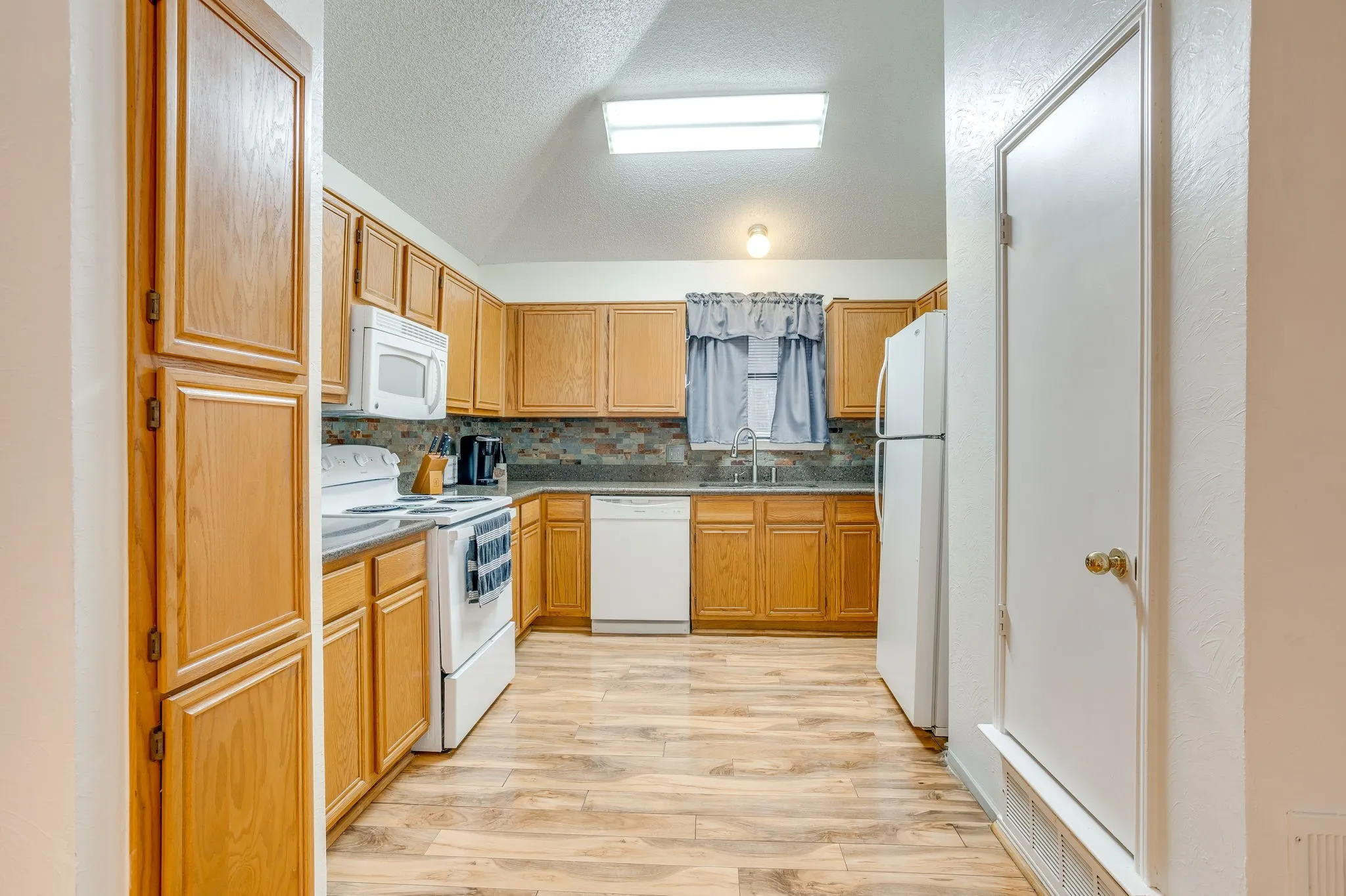 Kitchen featuring wood-finish flooring, oak cabinetry, white appliances, and a tiled backsplash