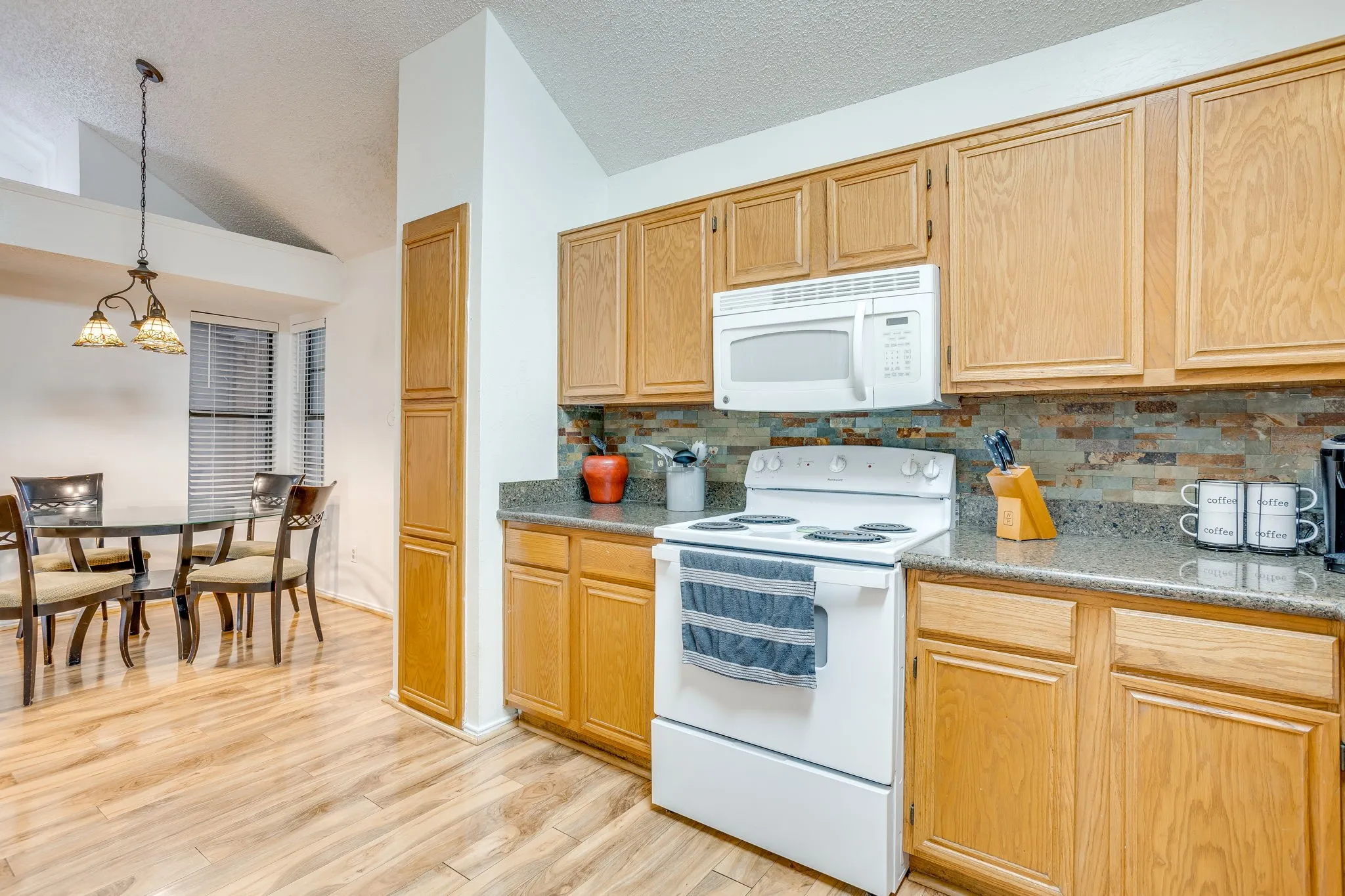 Vaulted ceilings, wood-finish flooring, wood cabinetry, stone-look backsplash, and built-in microwave