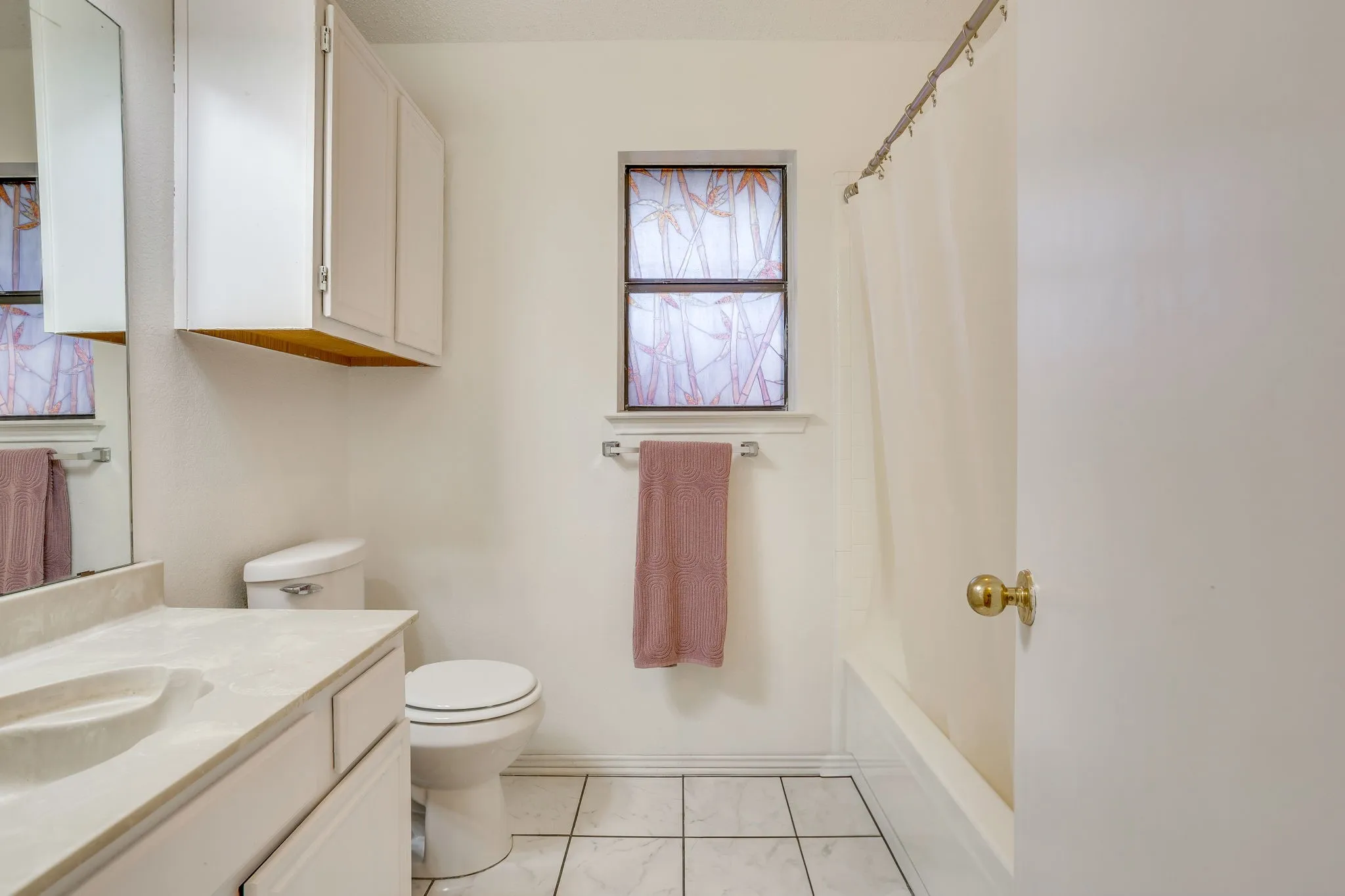 White tile flooring, a built-in vanity with an integrated sink, white cabinetry, and a bathtub with a shower curtain rod