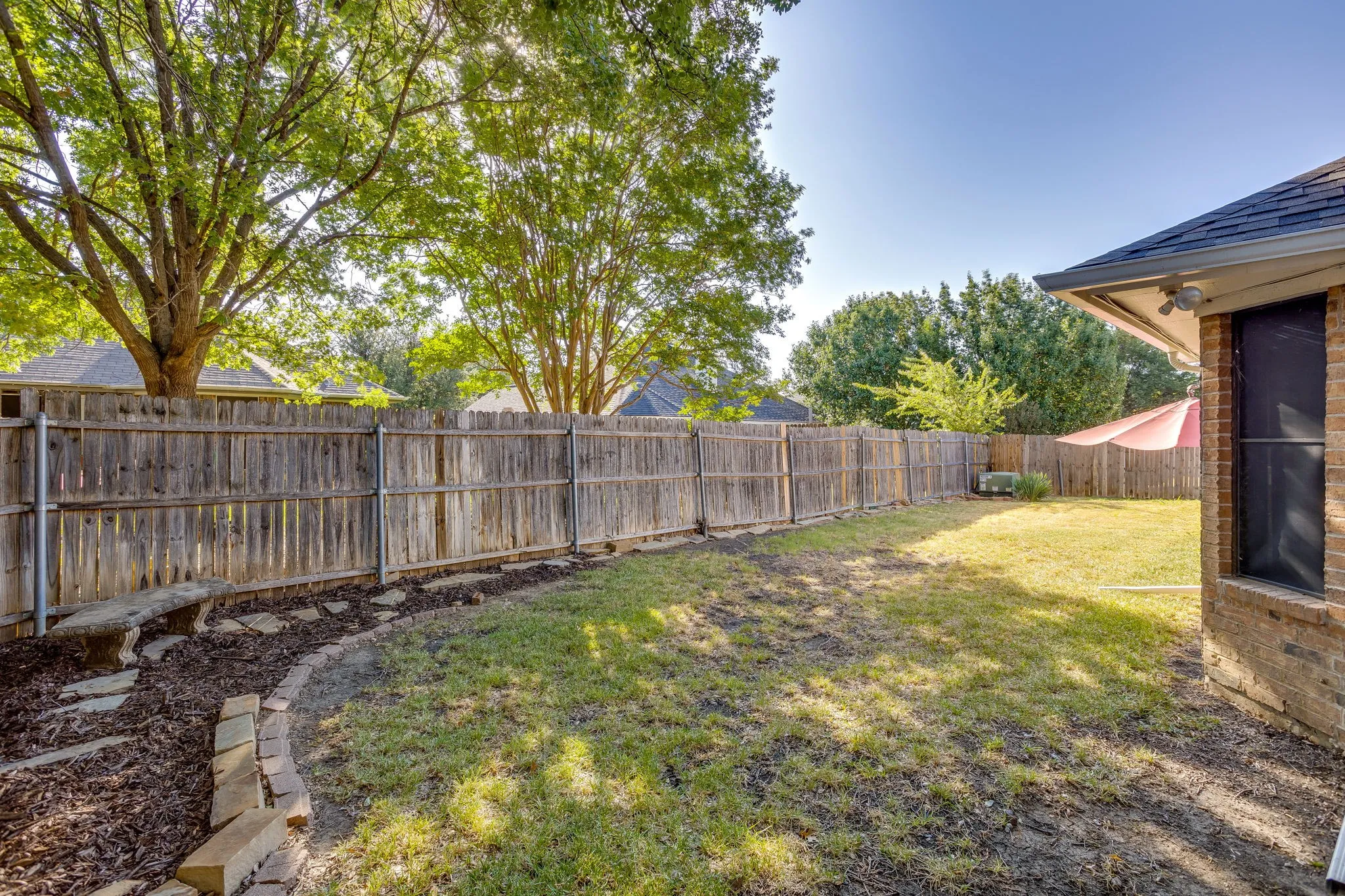 Expansive backyard oasis featuring a mature tree canopy, level lawn, wood-finish privacy fencing, and a brick utility structure