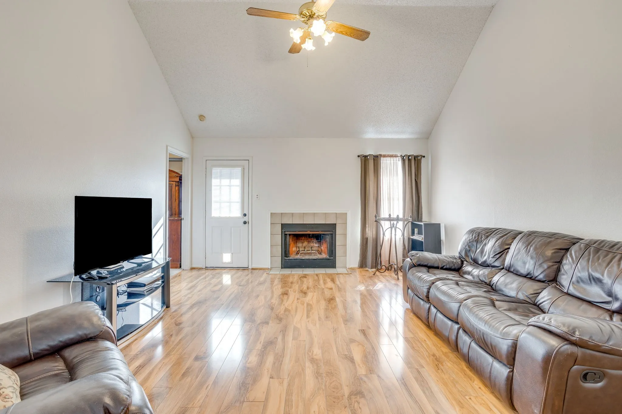 Vaulted ceiling, wood-finish flooring, fireplace with tile surround, ceiling fan, and white paneled door