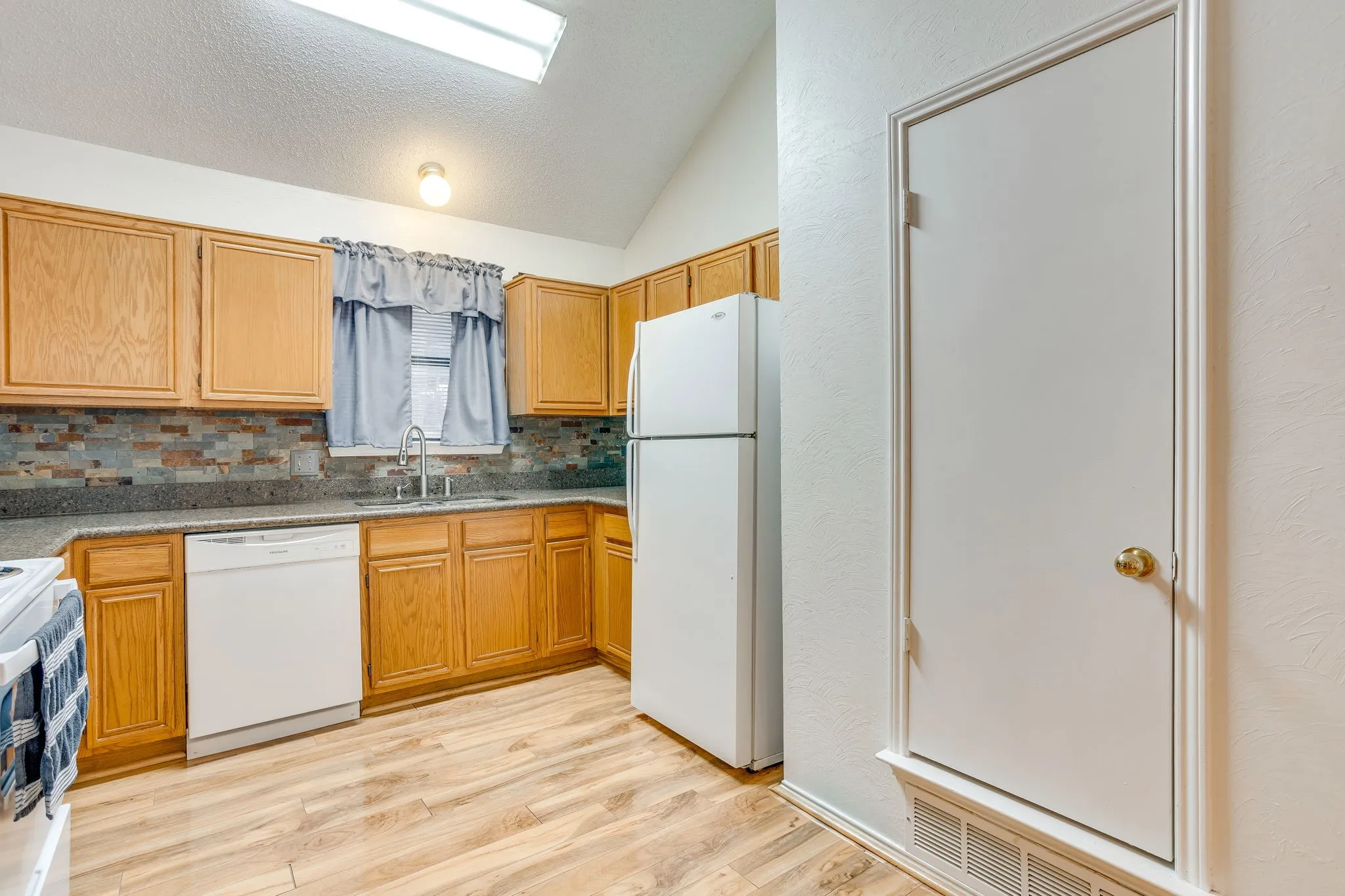 Kitchen featuring wood-finish cabinetry, a mosaic tile backsplash, composite countertops, a stainless steel sink, and wood-finish flooring