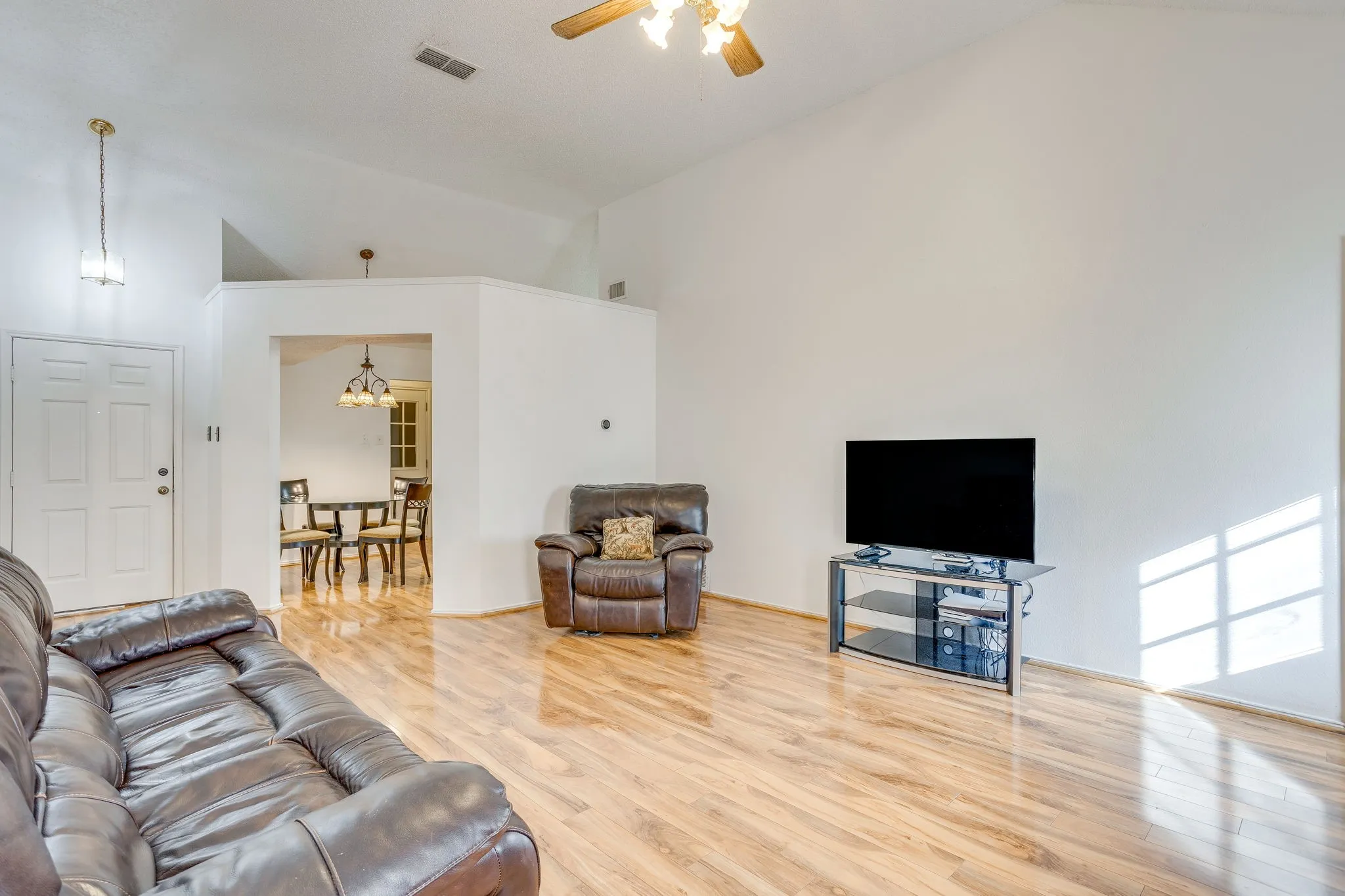 Vaulted ceiling with a ceiling fan, wood-finish flooring, recessed entry, and an open doorway