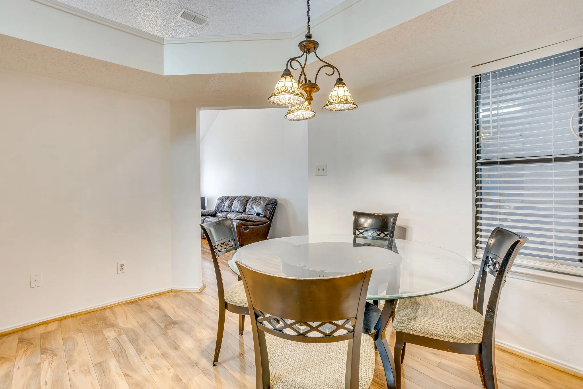 Vaulted ceiling with an ornate chandelier, wood-finish flooring, and a large window with blinds