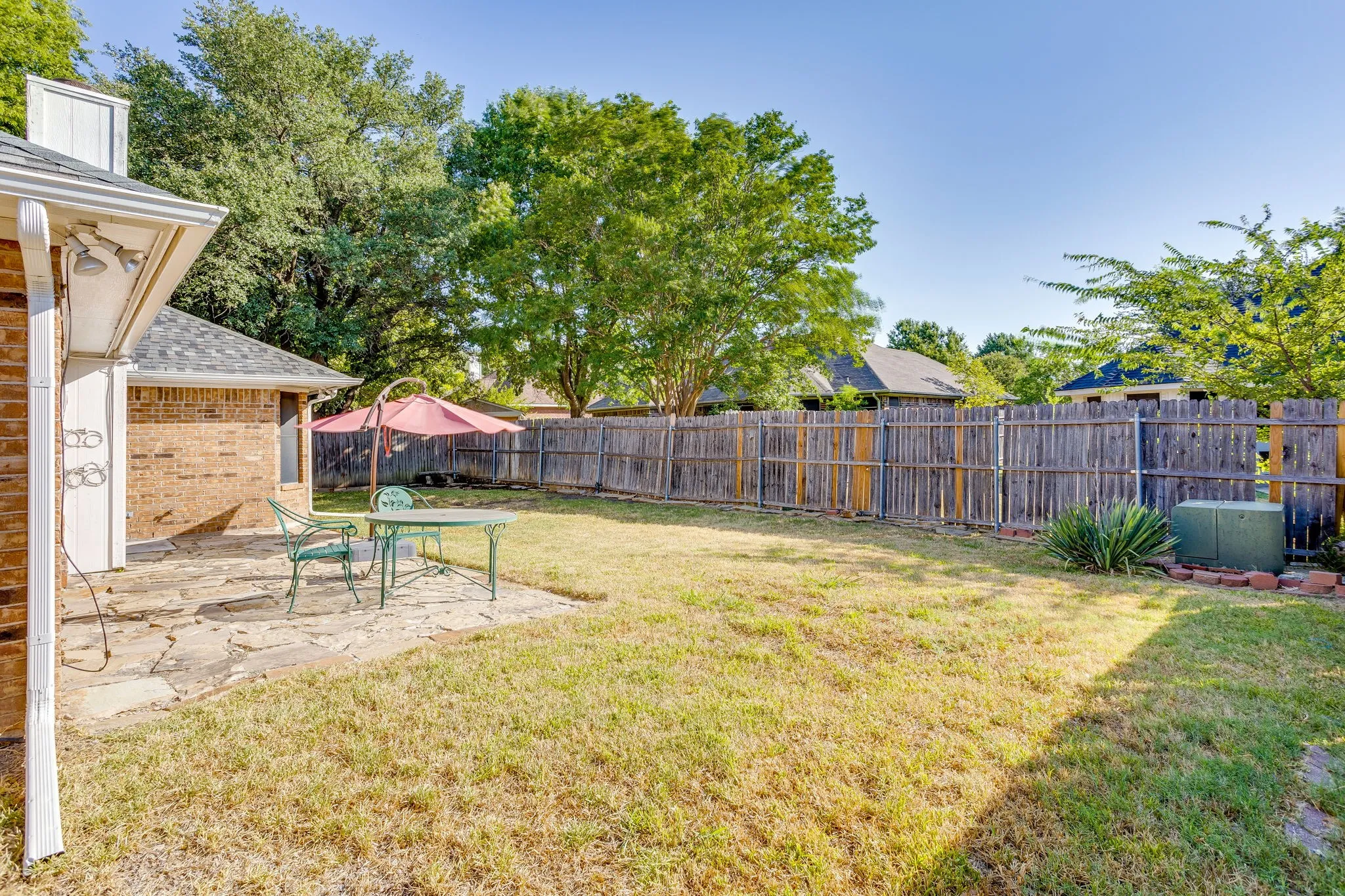 Expansive backyard featuring a stone patio, brick exterior, and wood privacy fencing