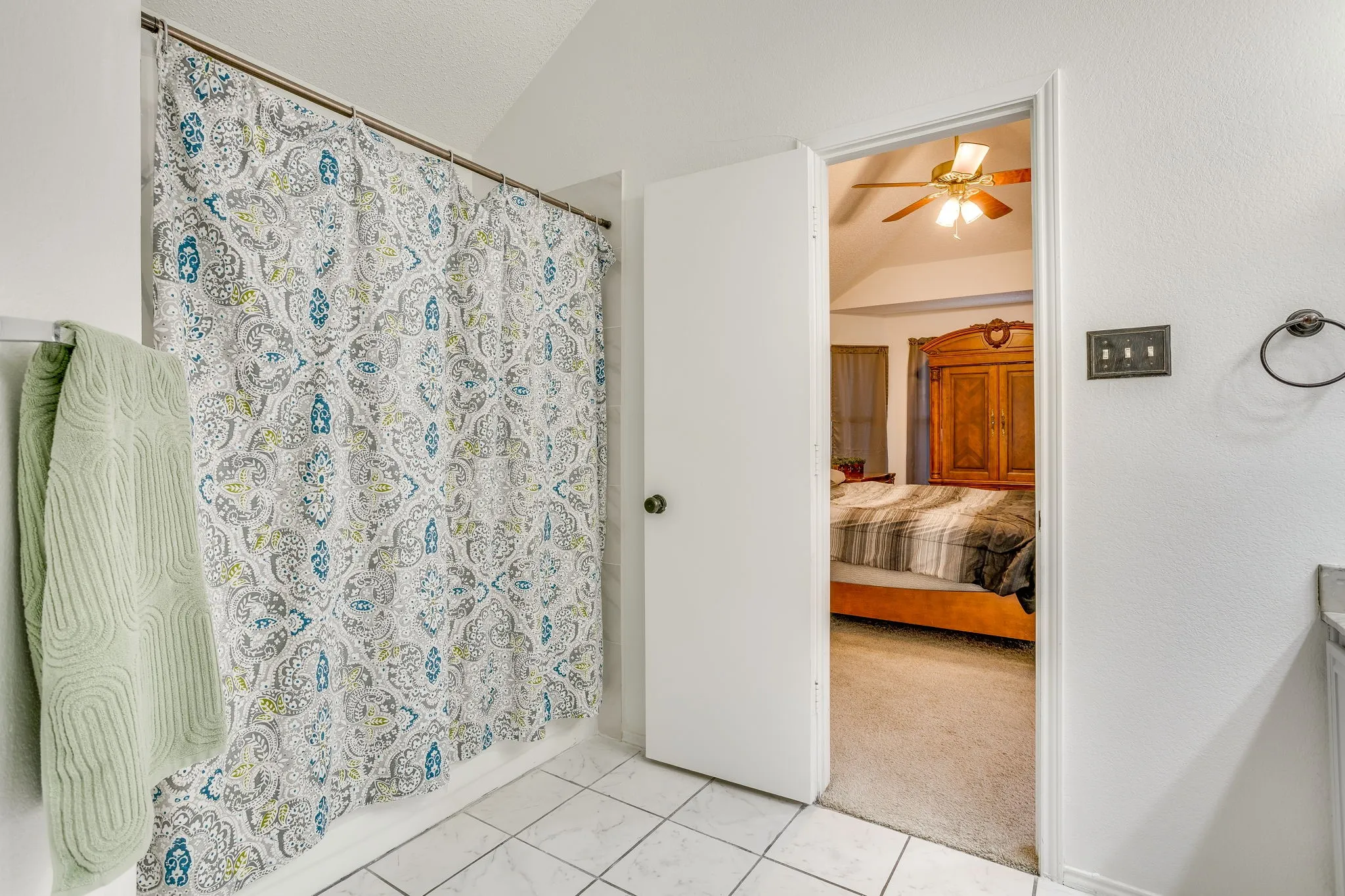 Primary bathroom featuring ceramic tile flooring, a decorative shower curtain with coordinating towel bar, and direct access to the adjoining bedroom through an open doorway