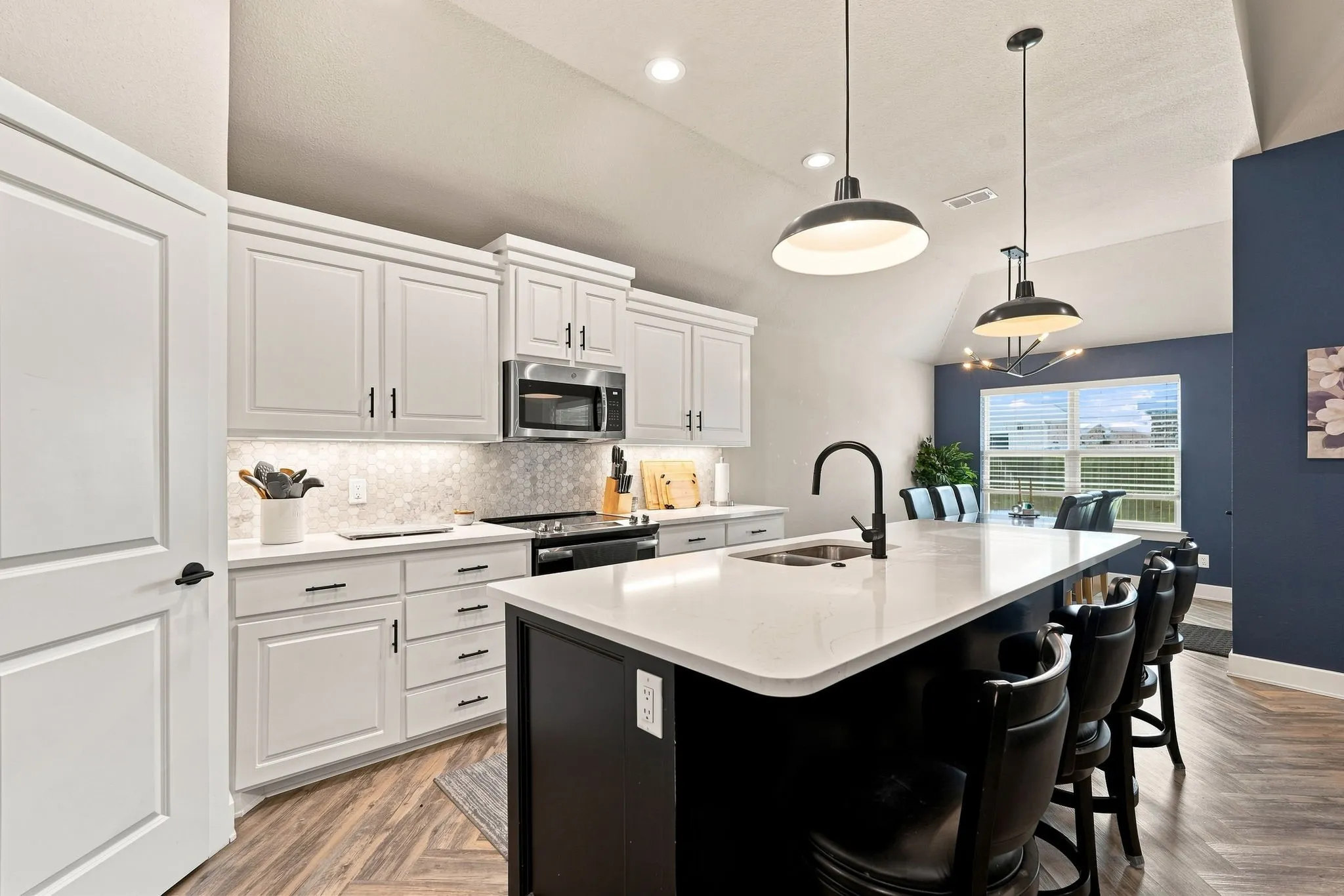 Kitchen featuring white cabinetry with dark hardware, stainless steel microwave, black range, and an expansive island with a white countertop and integrated sink