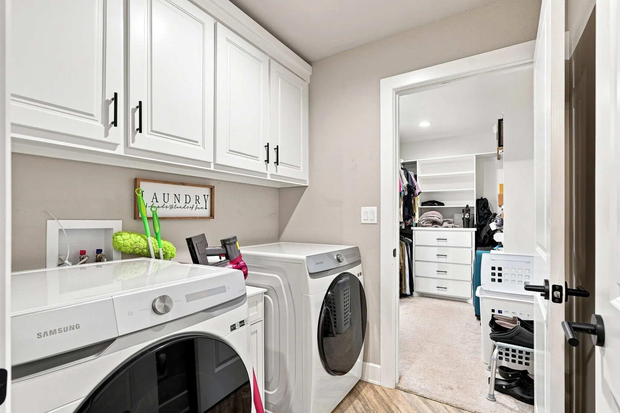 White shaker-style cabinetry with black hardware, wood-finish flooring, and a walk-in closet with built-in shelving