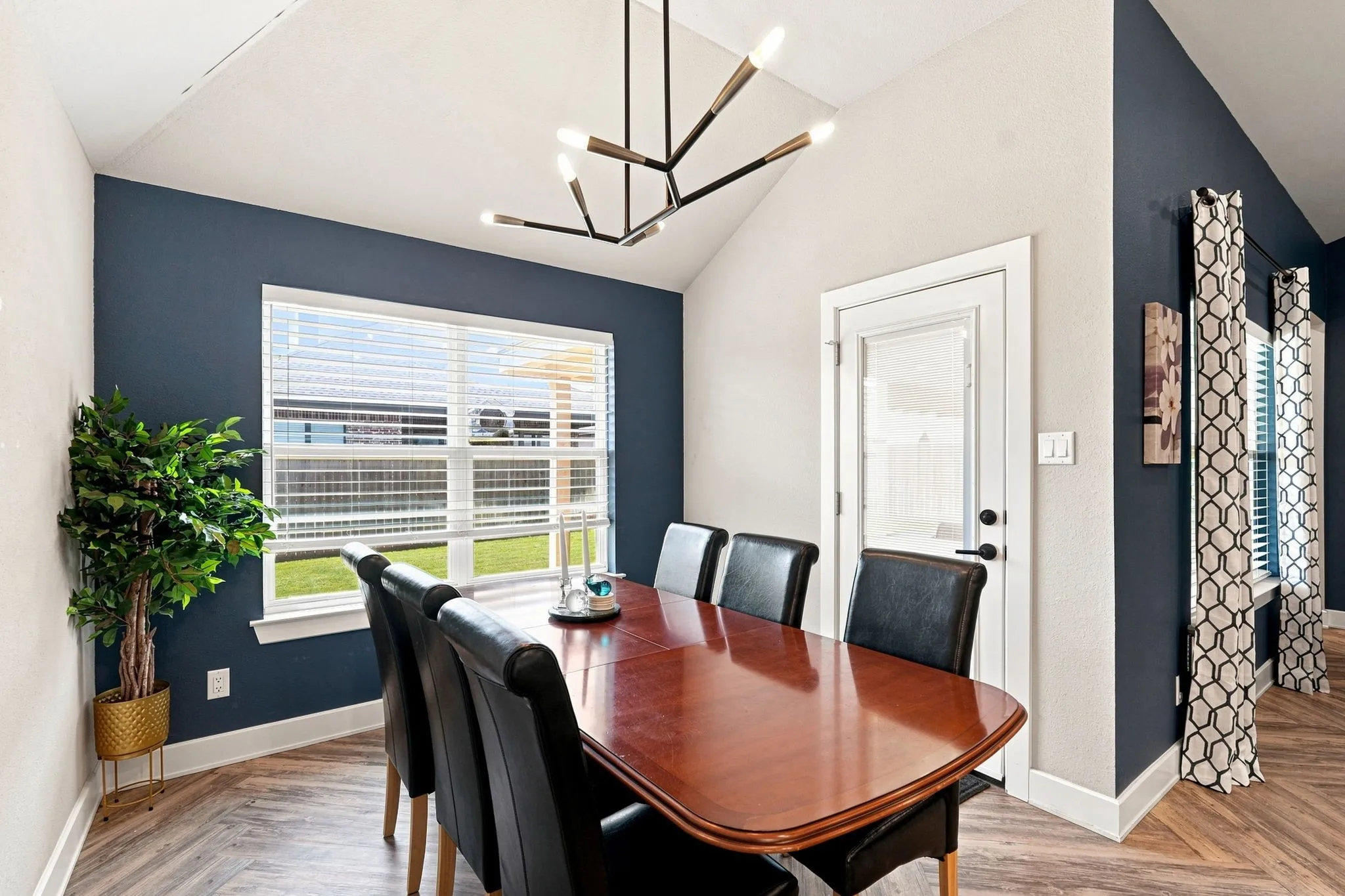 Vaulted ceiling, modern linear chandelier, wood-finish flooring, two-tone wall treatment, and a glass-paneled exterior door