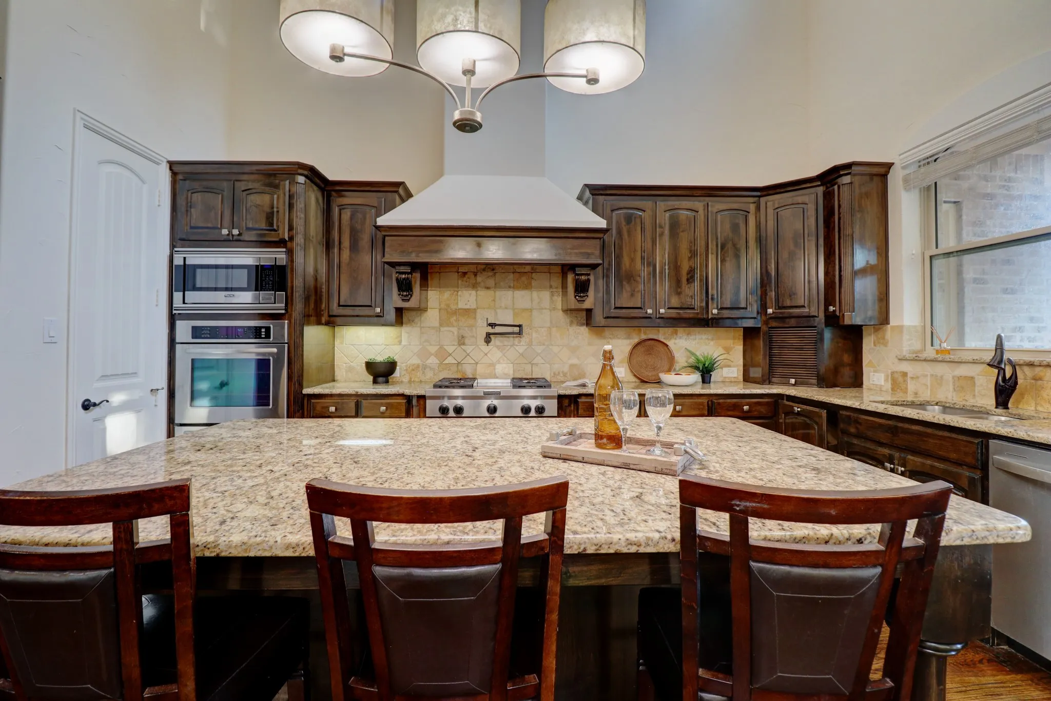 Kitchen featuring a granite island, coordinating countertops, dark wood cabinetry, stainless steel appliances, and a tile backsplash