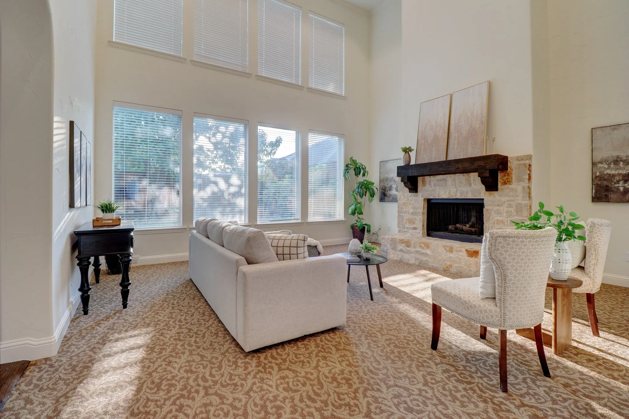 Living area featuring a stone fireplace with a wood mantle, high ceilings, multiple windows, and patterned carpeting