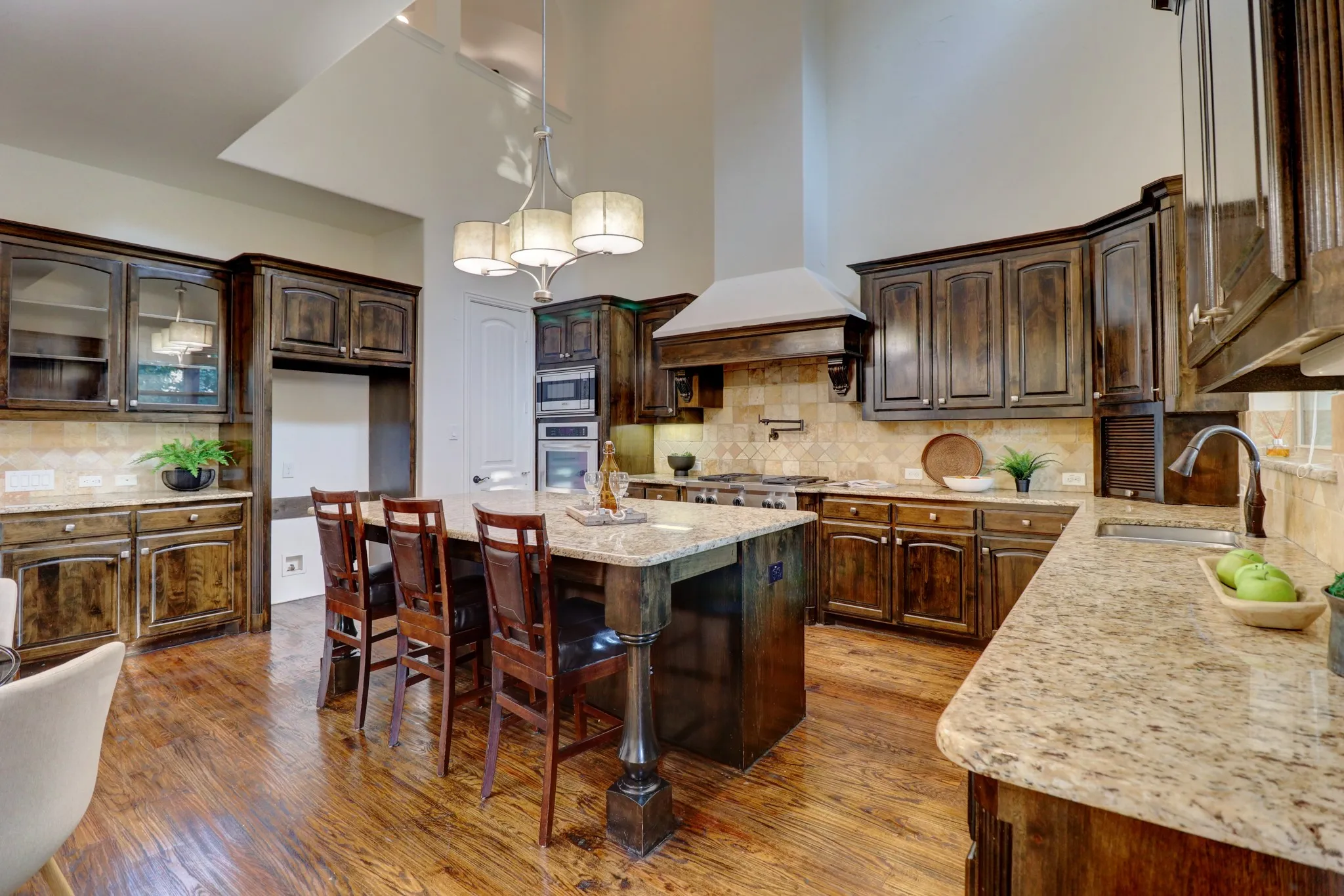 Spacious kitchen featuring rich wood cabinetry, granite countertops, wood-finish flooring, a central island with seating, and stainless steel appliances