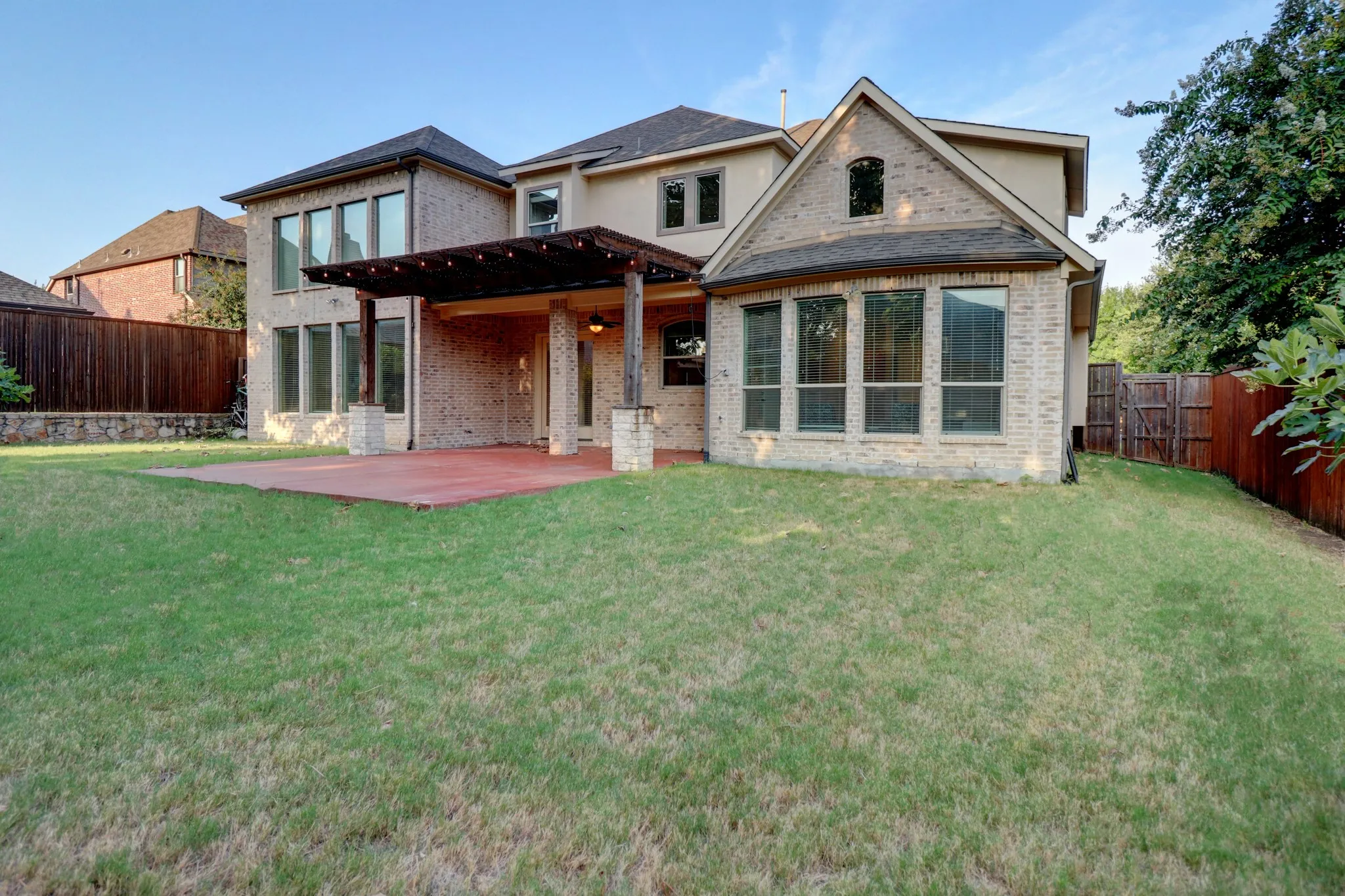 Brick and stucco exterior with multiple large windows, covered patio, wood pergola, and expansive lawn