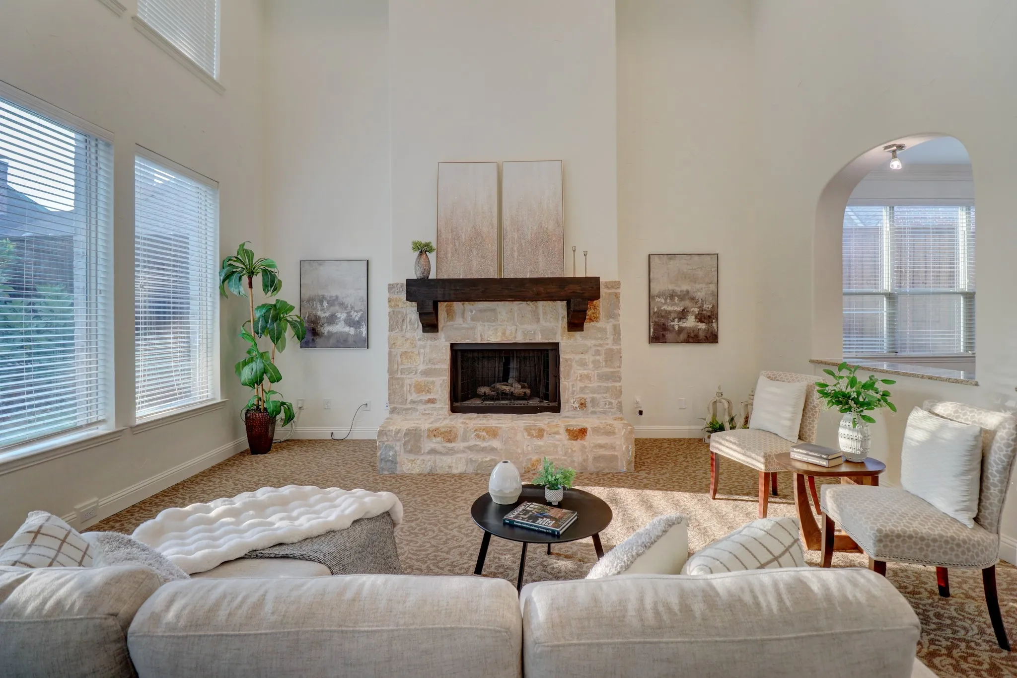 Two-story living area featuring a stone fireplace with a substantial wood mantel, high vaulted ceilings, and multiple windows