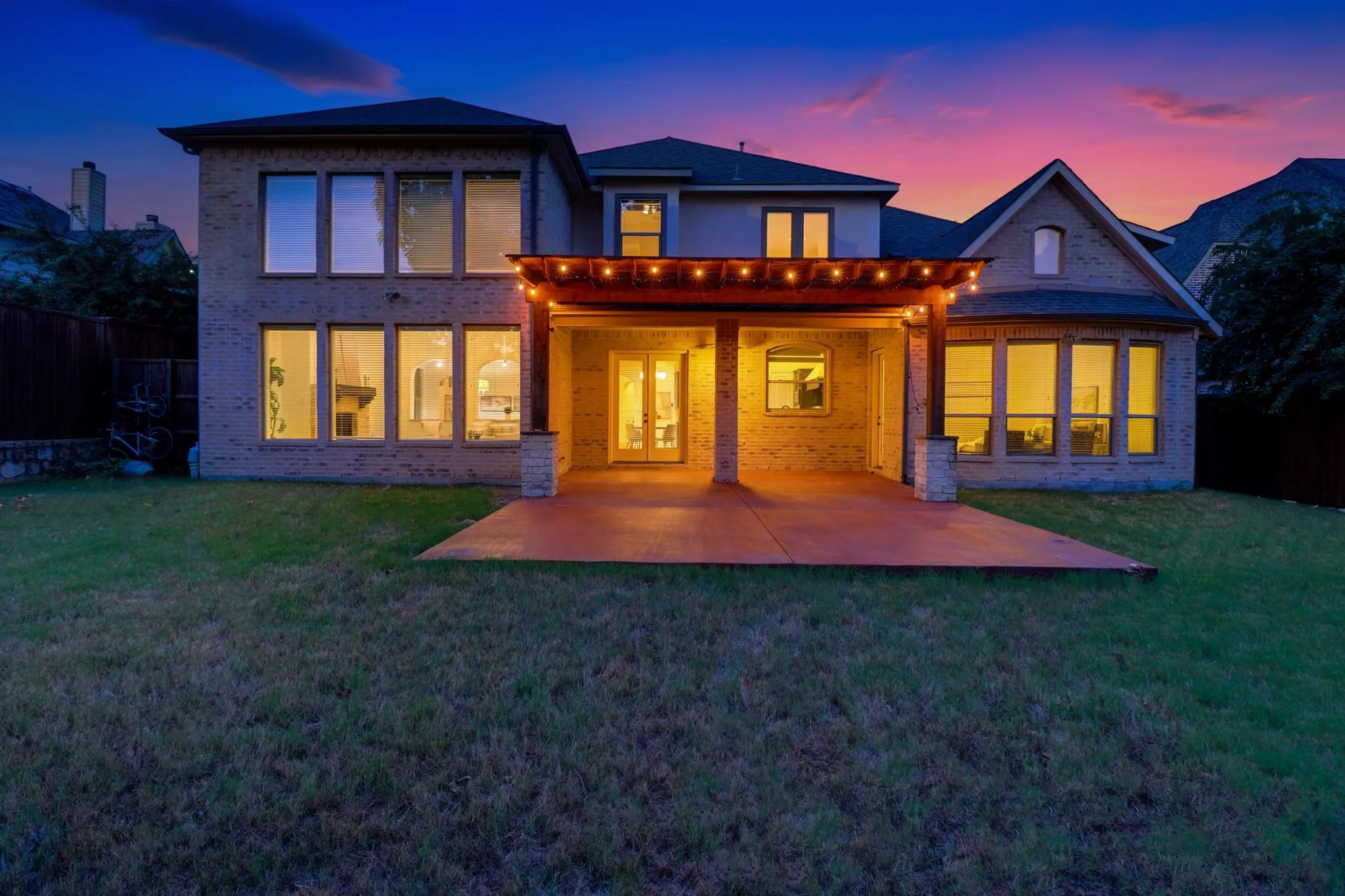 Brick exterior with multiple large windows, covered patio with wood pergola, and stone-clad columns