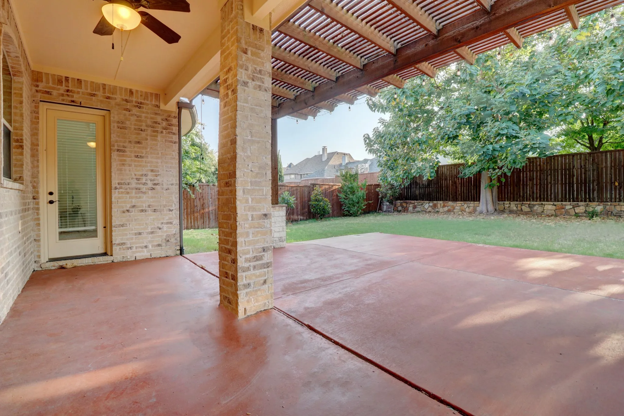 Expansive covered patio with wood-finish ceiling and ceiling fan, anchored by substantial brick columns
