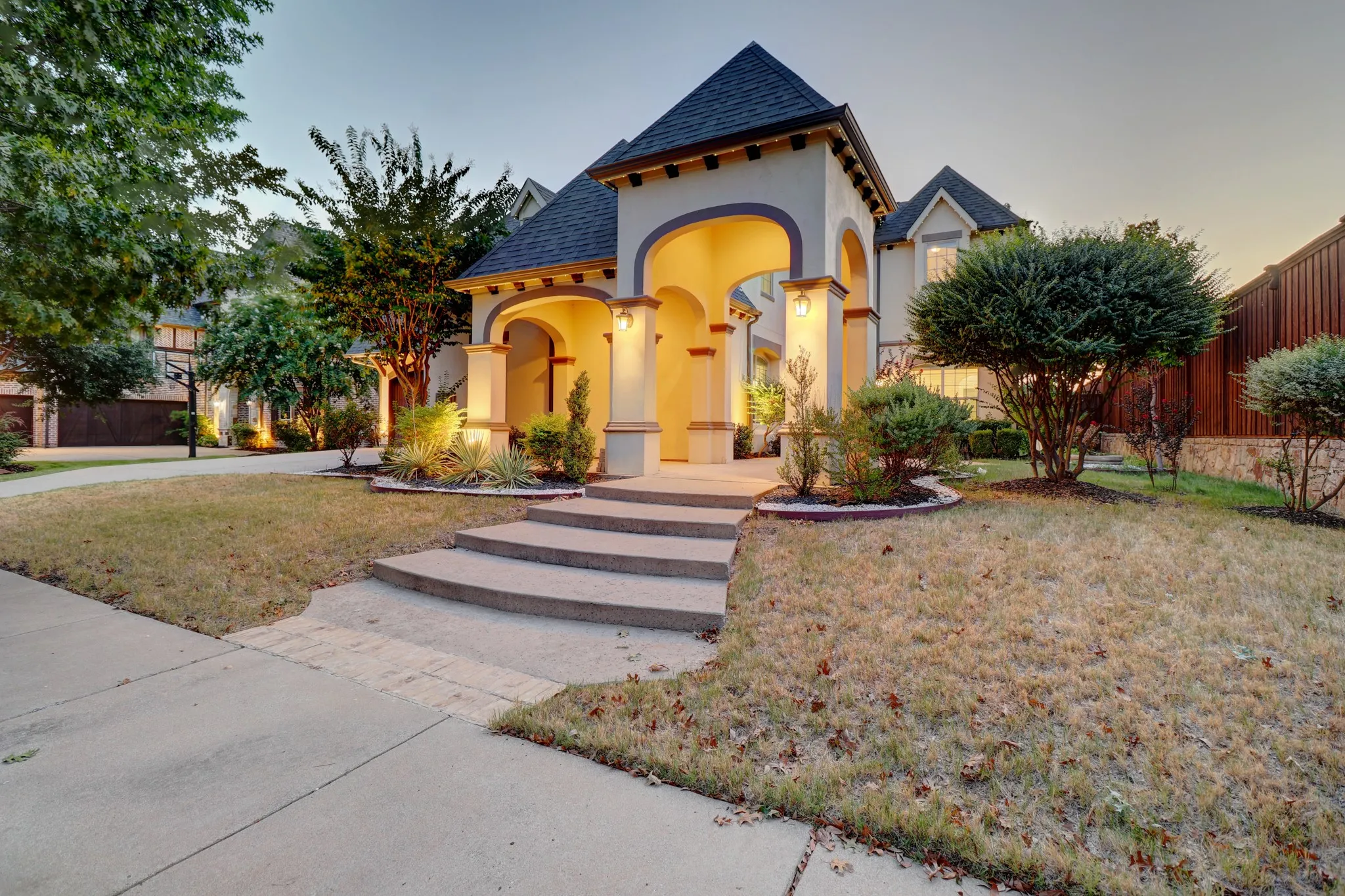 Stucco exterior with a grand arched entry, dark tile roof, and stone steps