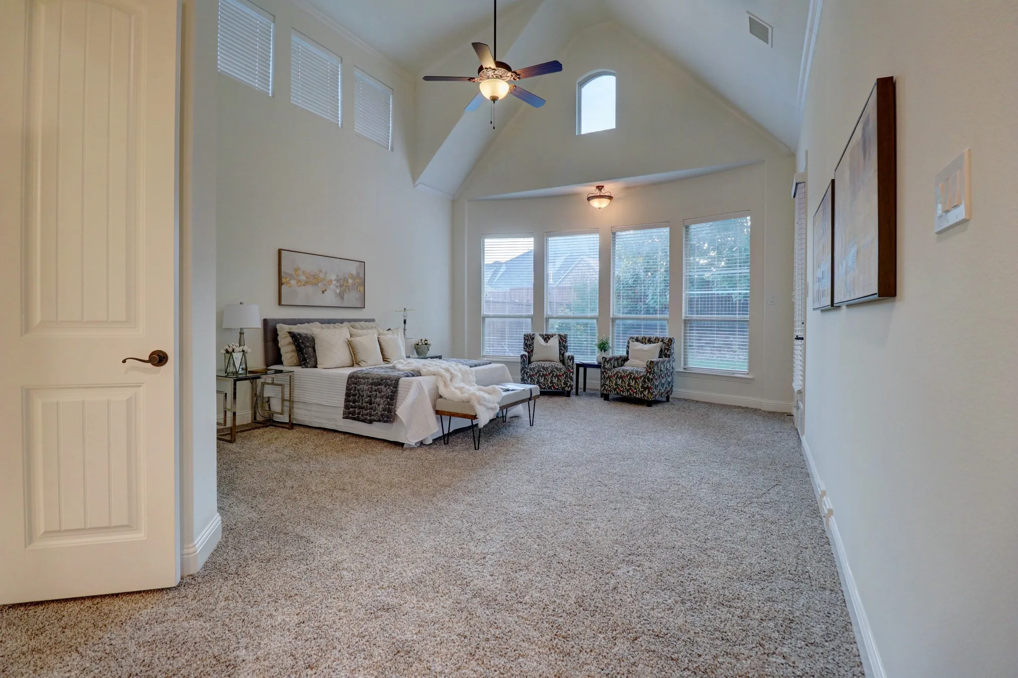 Vaulted ceiling with ceiling fan, arched transom window, recessed bay window area, and neutral carpet flooring