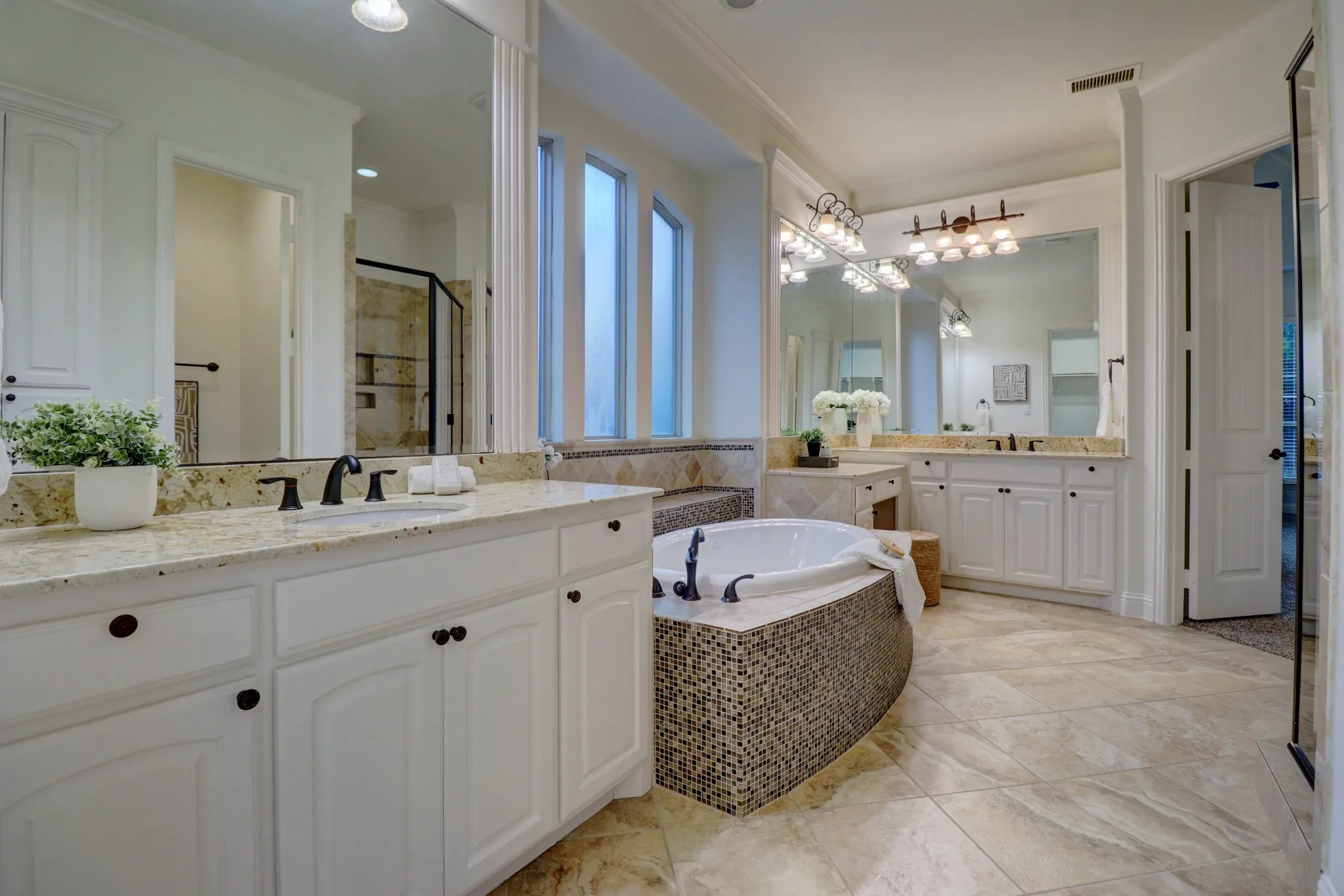 Built-in soaking tub with mosaic tile surround, two separate vanity stations with white cabinetry, granite countertops, and tile flooring