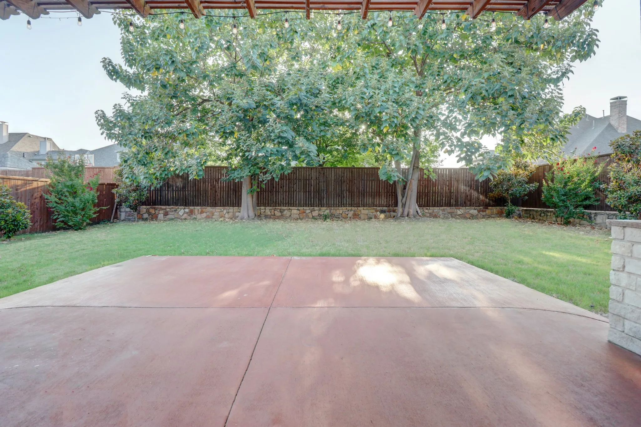 Expansive backyard featuring a large concrete patio, manicured lawn, and mature trees