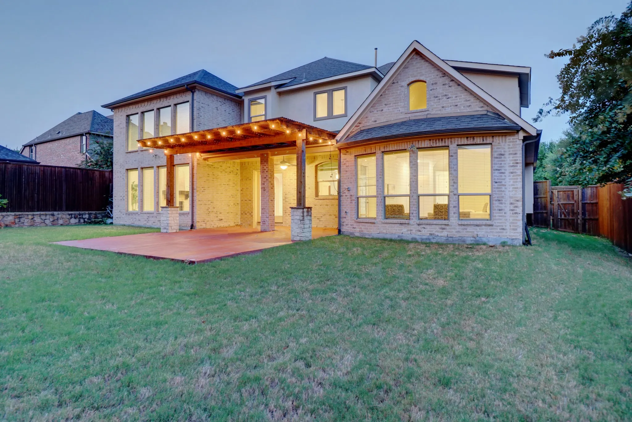 Expansive backyard featuring a brick exterior, covered patio with a wood pergola, and large windows