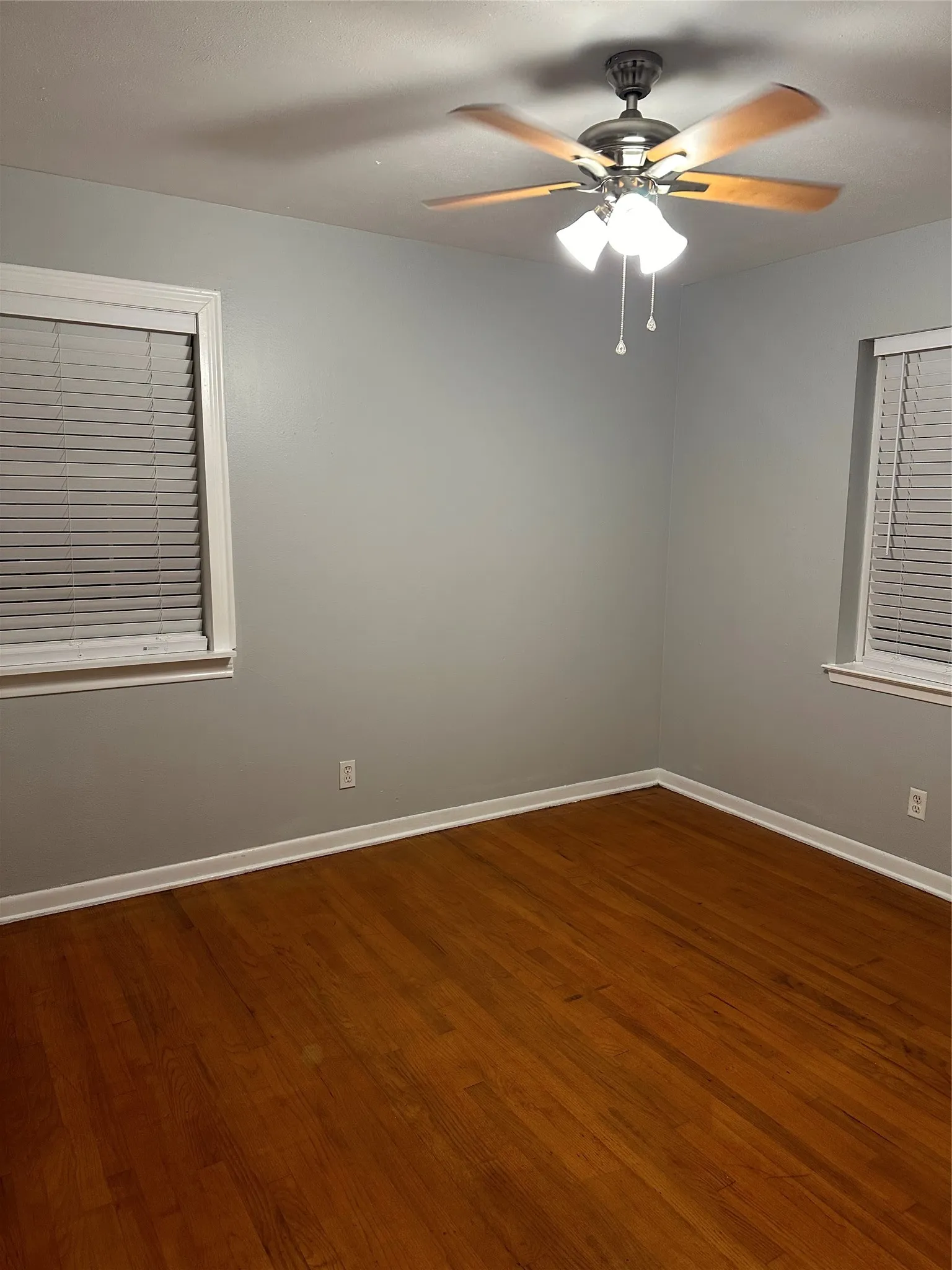 Wood-finish flooring, two windows with blinds, ceiling fan with integrated lighting, and neutral wall paint