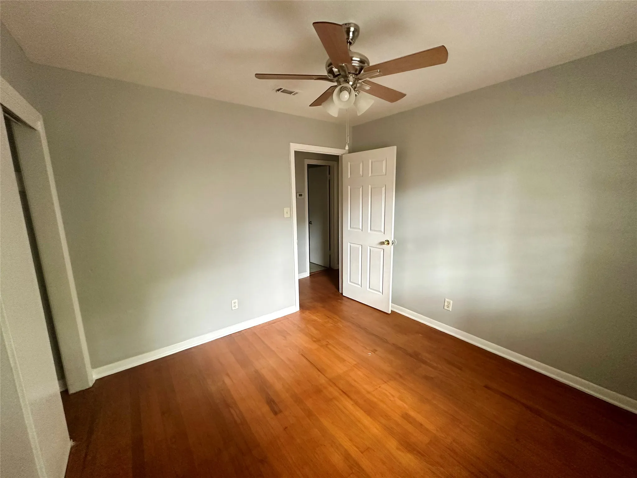 Hardwood-finish flooring, light gray wall color, white trim, paneled interior door, and a ceiling fan with integrated lighting