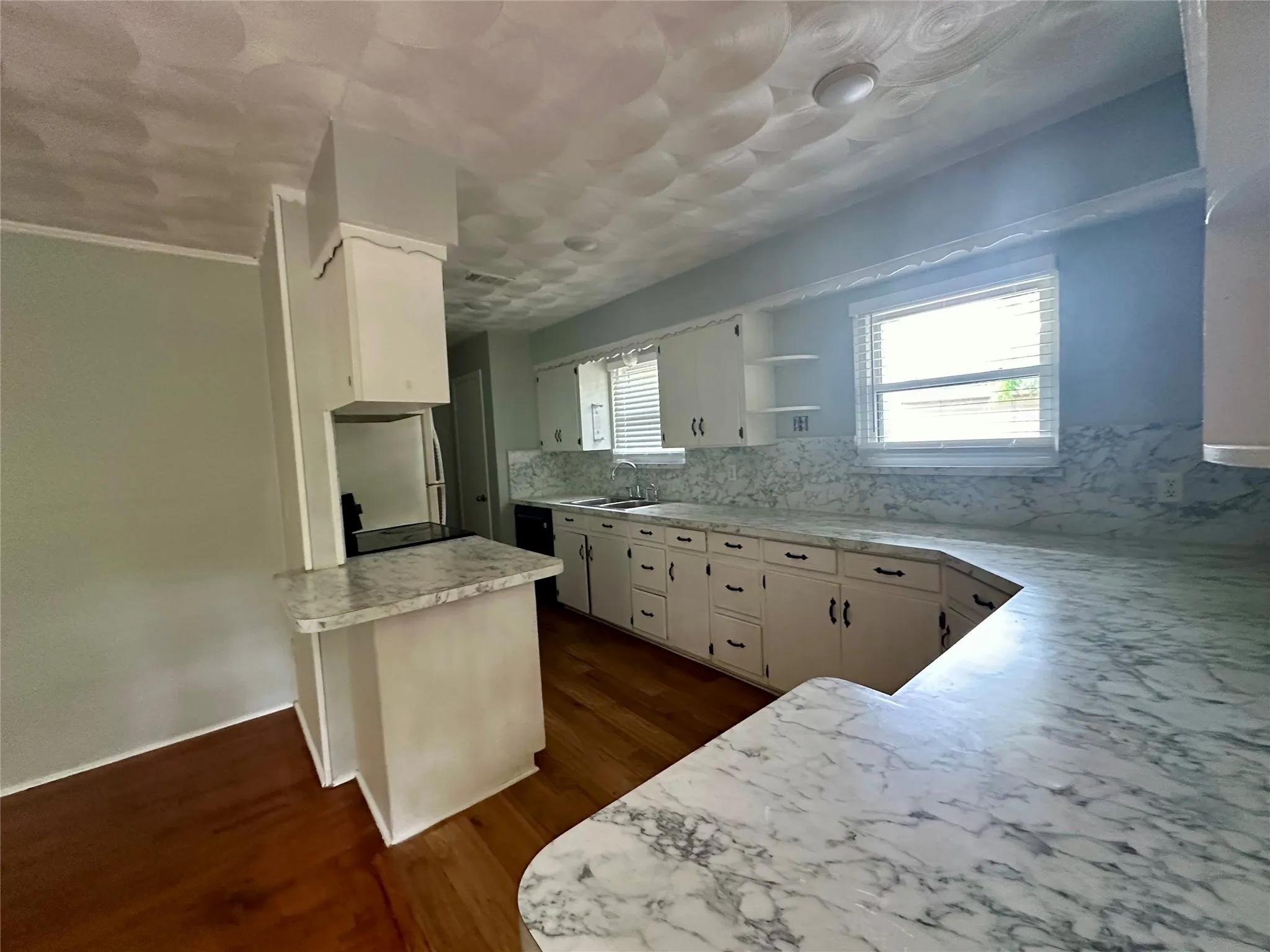 Kitchen featuring extensive white cabinetry, light-toned countertops with a marbled pattern, and wood-finish flooring