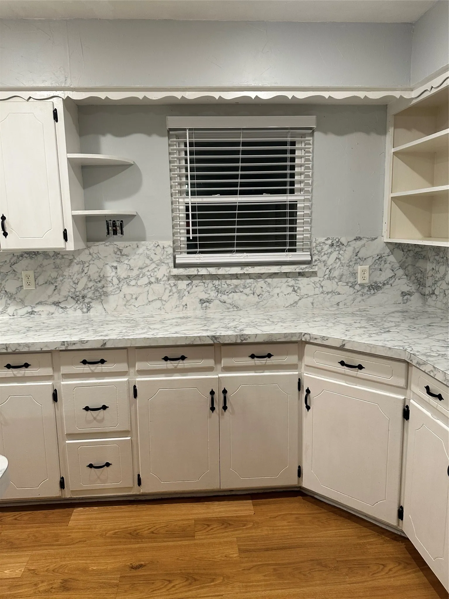White cabinetry with black hardware, corner shelving, wood-finish flooring, and white and gray patterned countertops