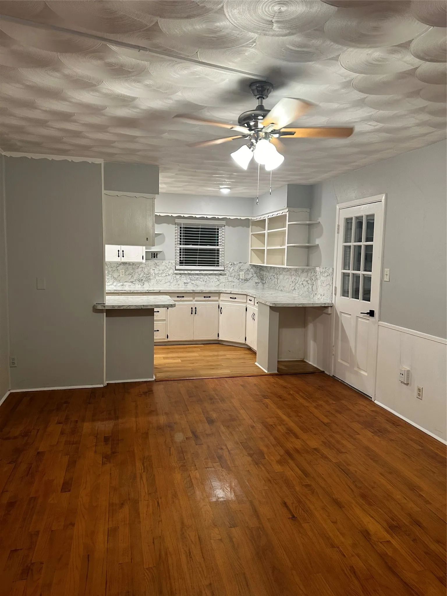 Wood-finish flooring, white cabinetry, light countertops, beaded wainscoting, and a ceiling fan with integrated lighting