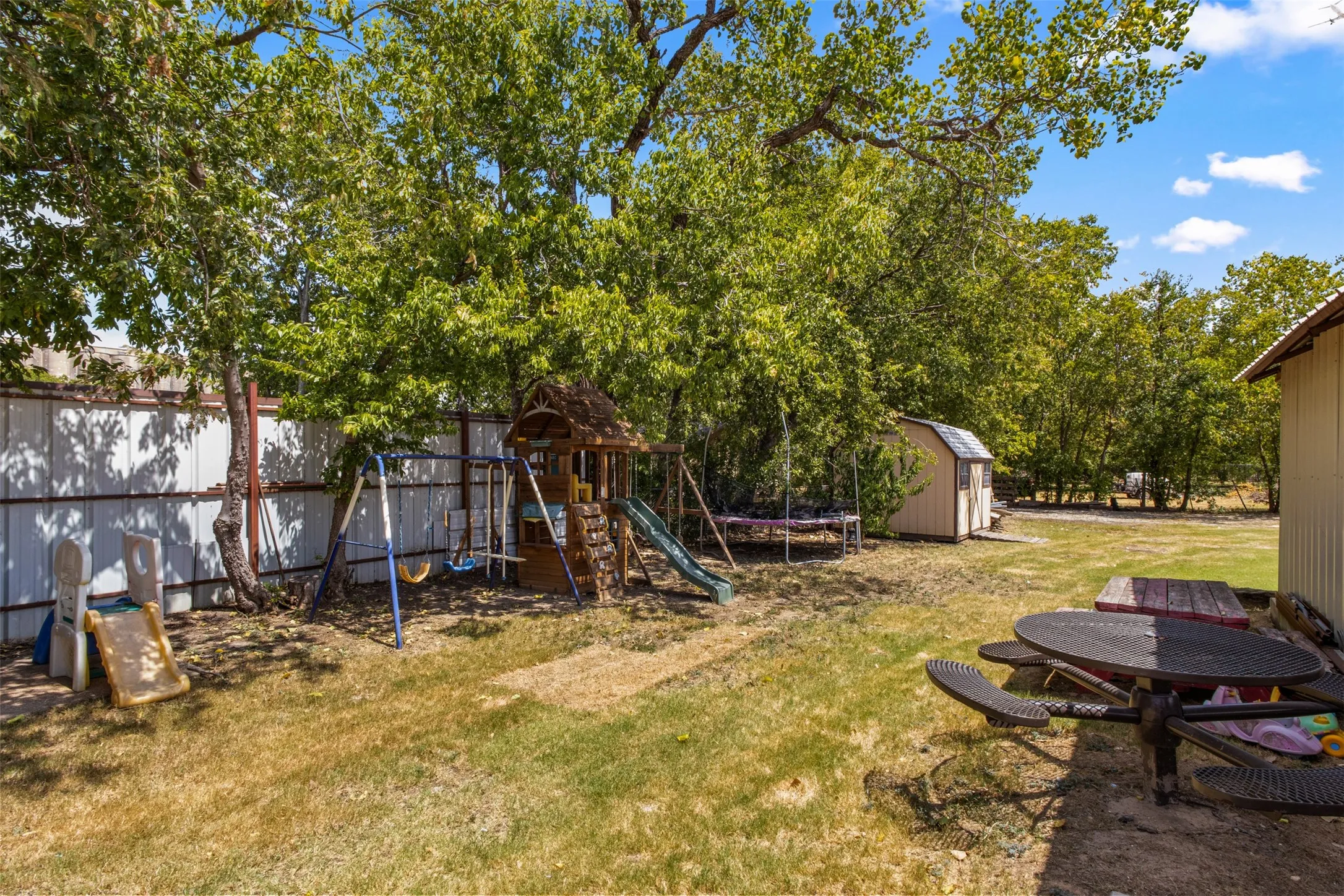Spacious outdoor area with mature trees, a detached storage shed, and perimeter fencing