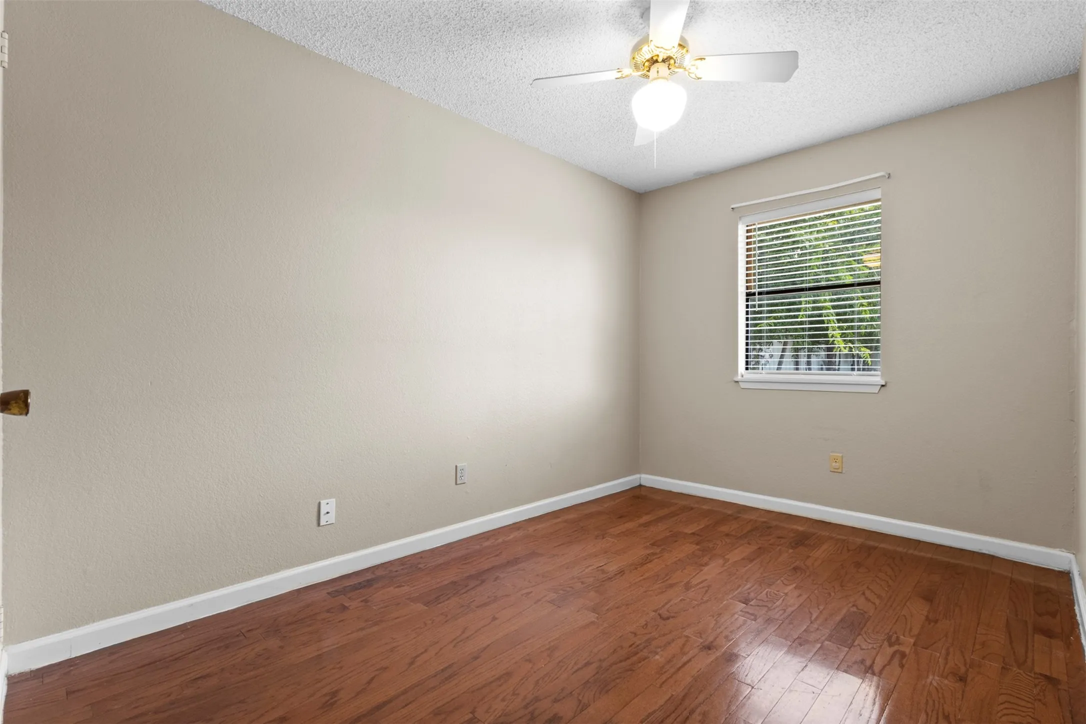 Hardwood flooring, neutral wall tones, window with horizontal blinds, and a ceiling fan with integrated lighting