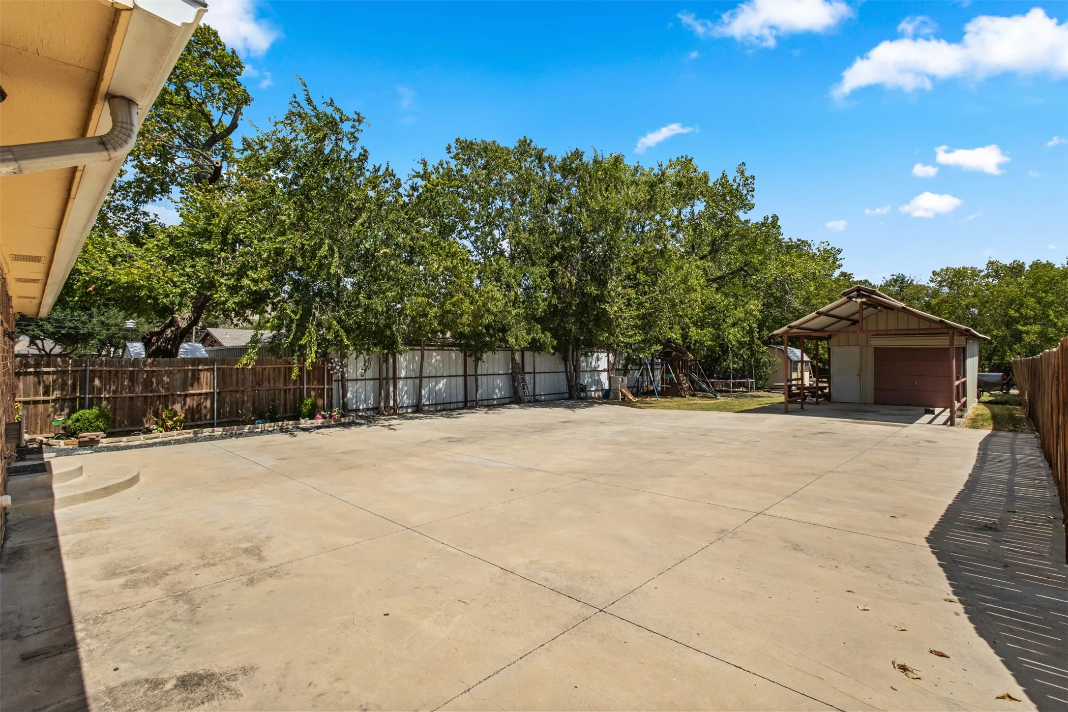 Expansive concrete patio with a detached outbuilding featuring a covered porch and garage door
