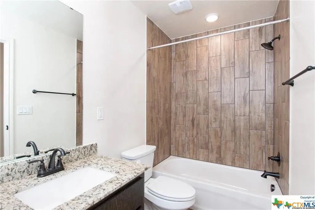 Bathroom featuring a granite countertop vanity with an undermount sink and dark bronze fixtures, a rectangular mirror, and a tub-shower combination with wood-look tile surround