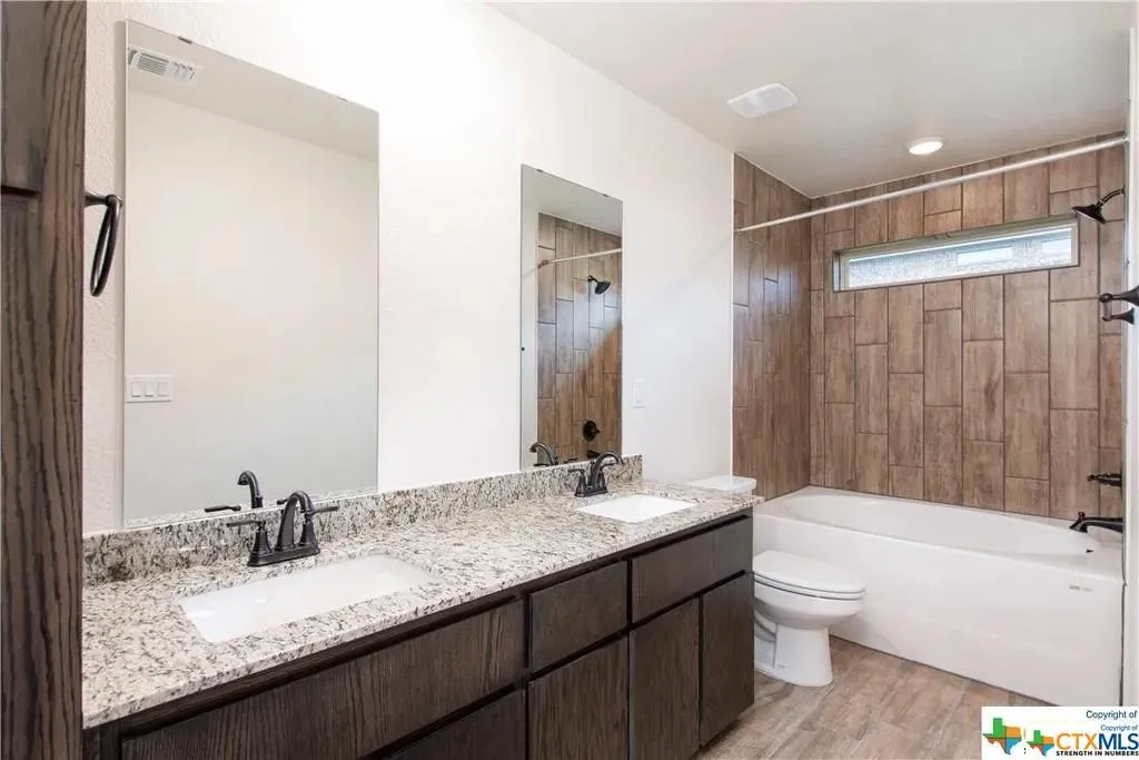 Bathroom featuring a dual vanity with a speckled countertop, integrated sinks, and dark wood-finish cabinetry