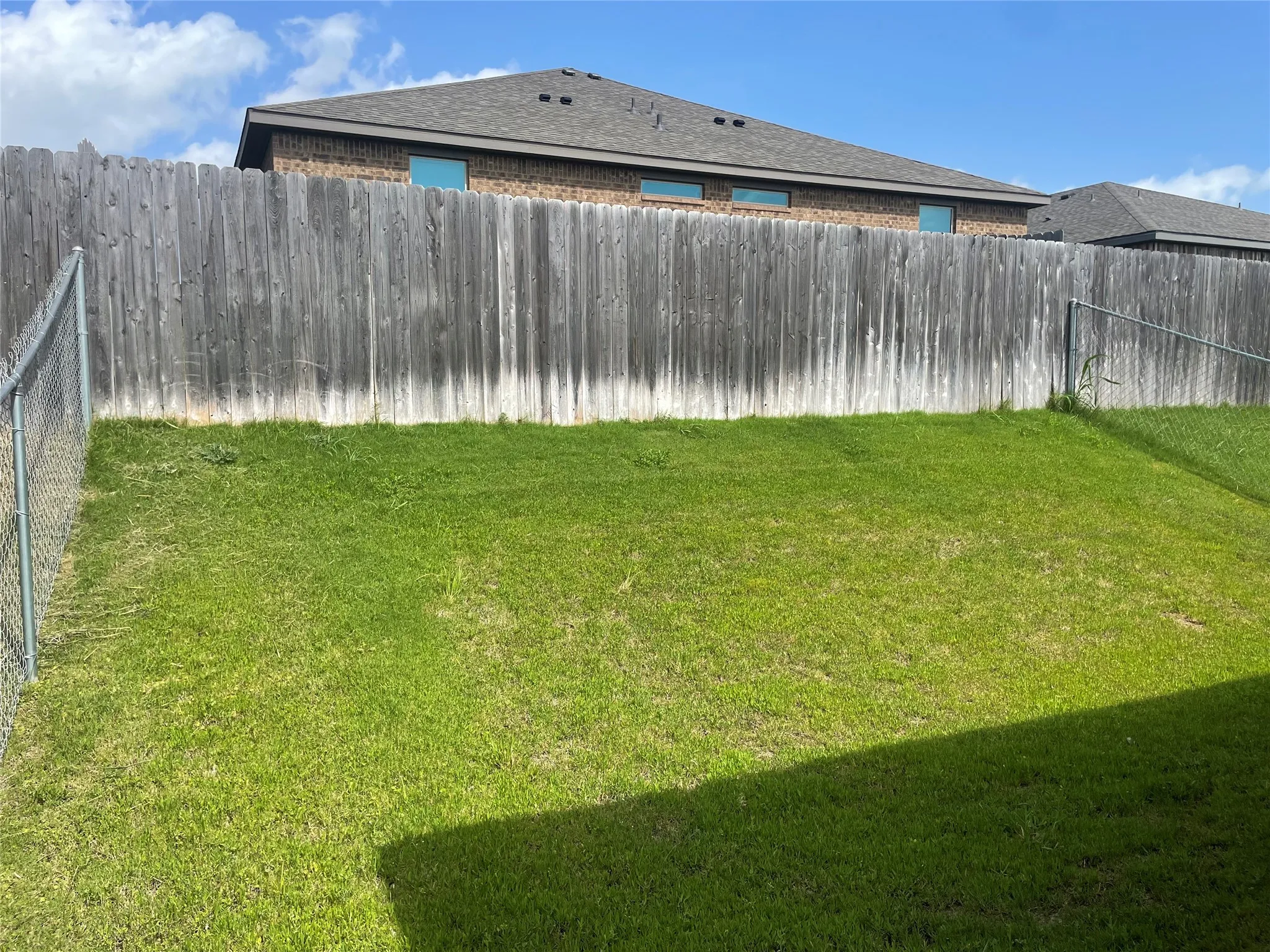 Expansive backyard featuring a lush green lawn, a tall wood privacy fence, and a chain-link fence on one side