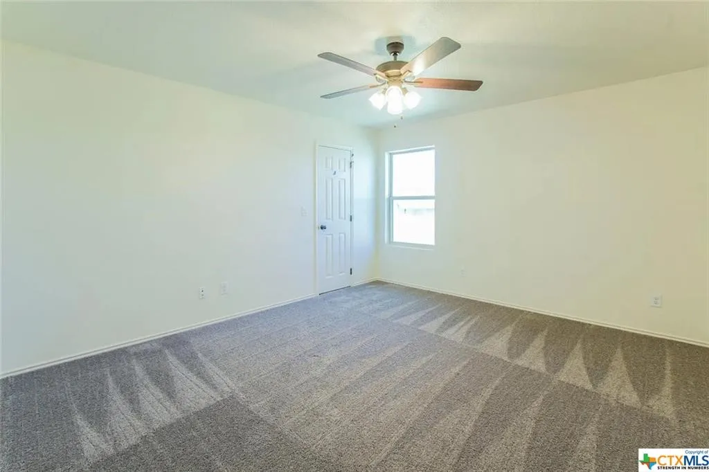 Spacious room featuring neutral carpeting, light-toned walls, and a ceiling fan with integrated lighting