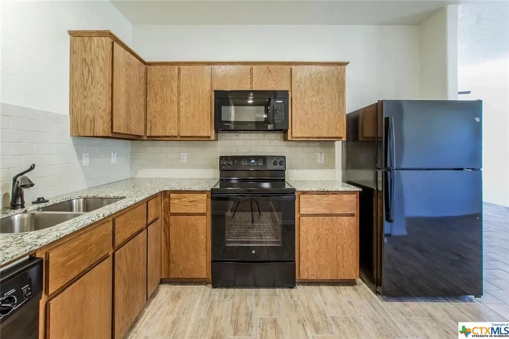 Kitchen featuring wood cabinetry, light-toned granite countertops, white subway tile backsplash, and light wood-finish flooring