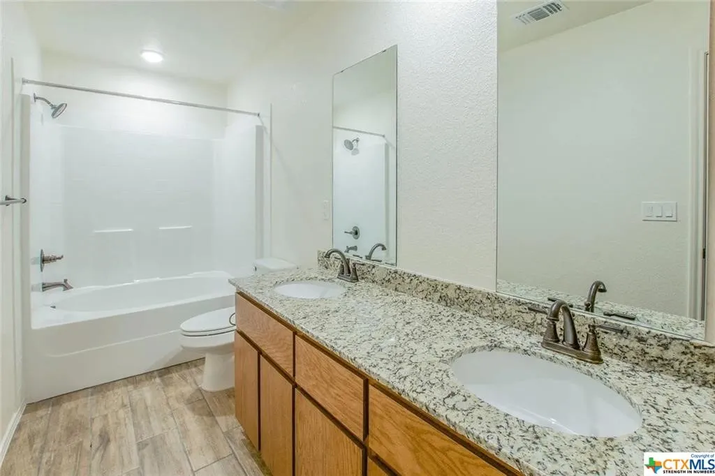 Bathroom featuring a double vanity with granite countertop, wood-finish cabinetry, dual undermount sinks, and bronze-finish fixtures