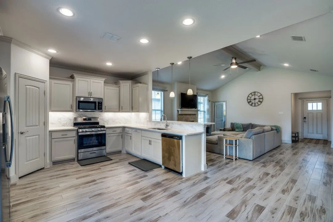 Spacious open-concept living area featuring wood-finish flooring, vaulted ceilings, and recessed lighting