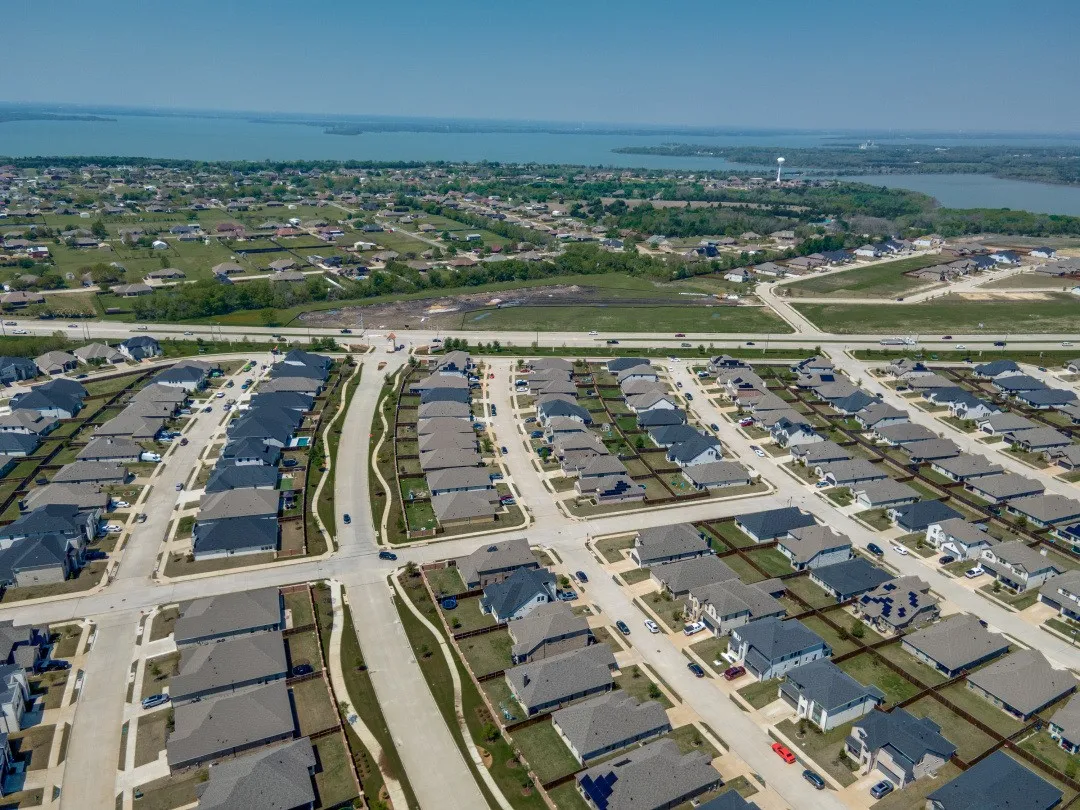 Aerial perspective of a developed residential community with dark-pitched roofs, adjacent to a large body of water