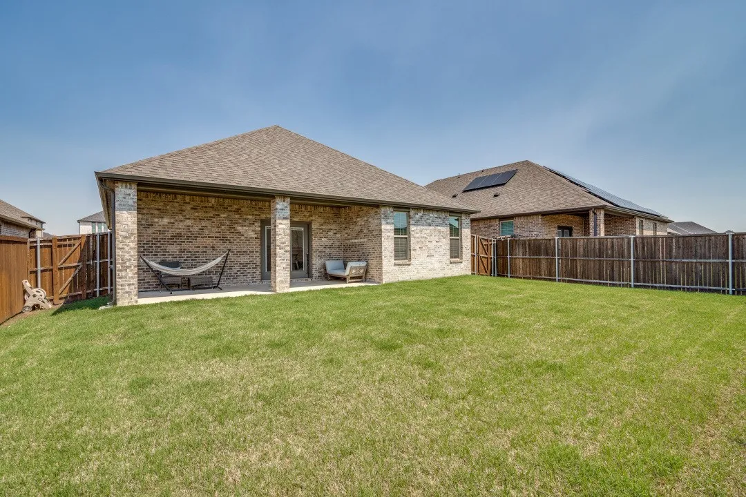 Expansive backyard featuring a covered patio, brick exterior, and a manicured lawn