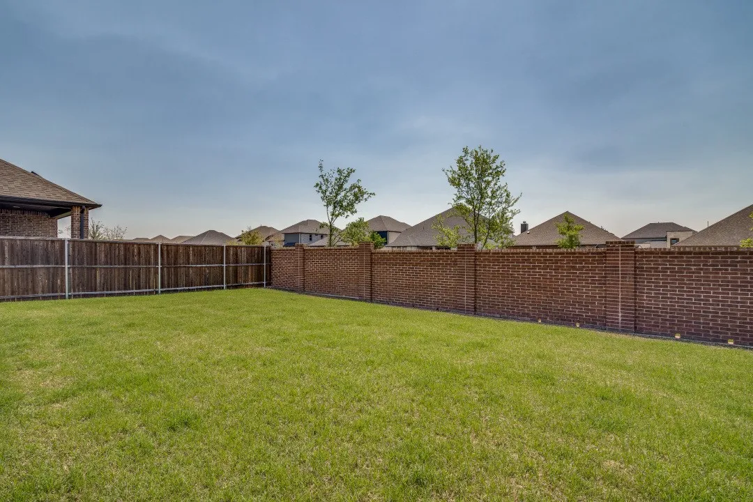 Expansive green lawn with a wood-fenced perimeter and a brick privacy wall
