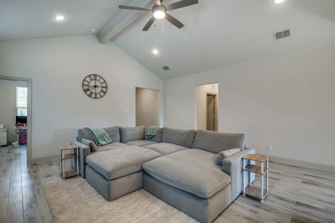 Vaulted ceiling with exposed beam, recessed lighting, ceiling fan, and wood-finish flooring
