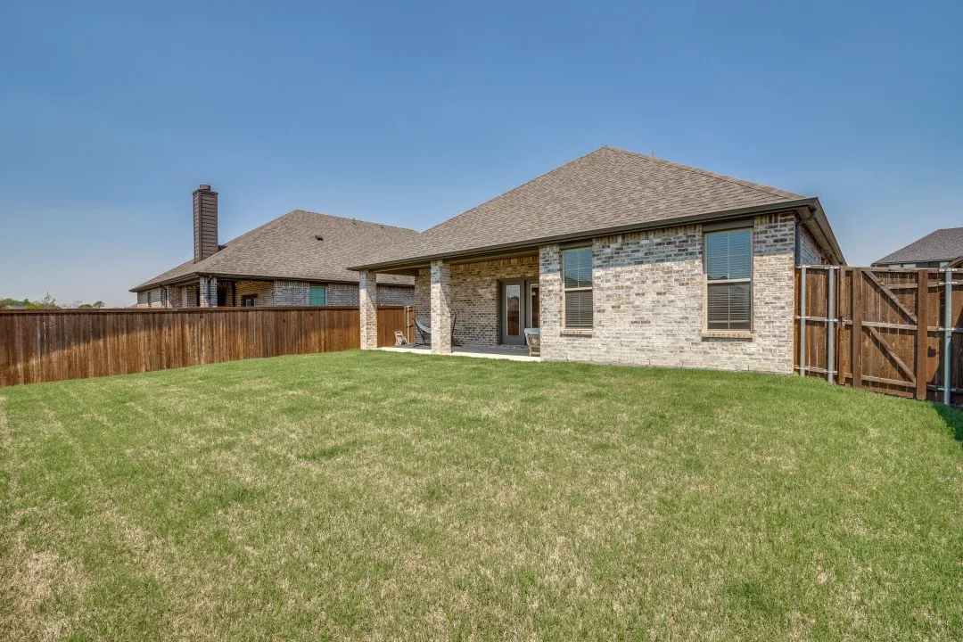Expansive backyard featuring a manicured lawn, full wood-plank fencing, and a covered patio with stone pillars