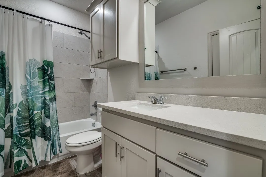 Bathroom featuring a shower-tub combination with tile surround, a built-in vanity with a single basin sink, a large wall-mounted mirror, and wood-finish flooring