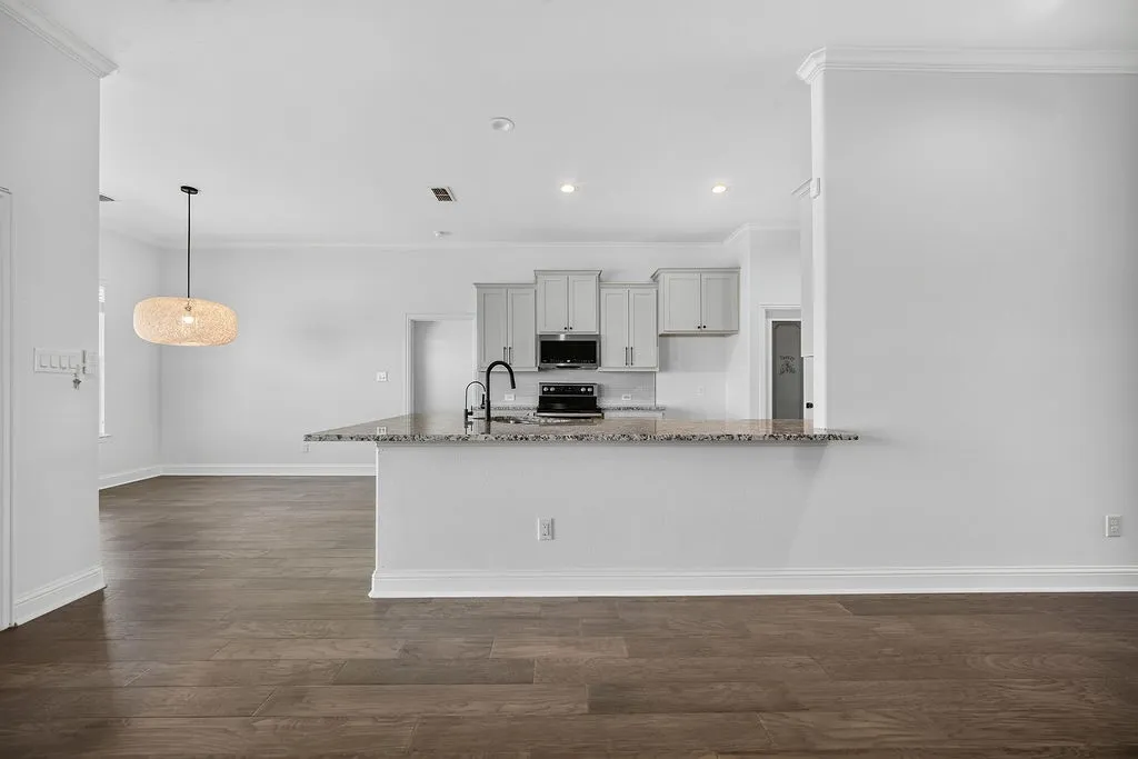Wood-finish flooring throughout, crown molding, kitchen with light gray cabinetry, built-in microwave, and a black faucet