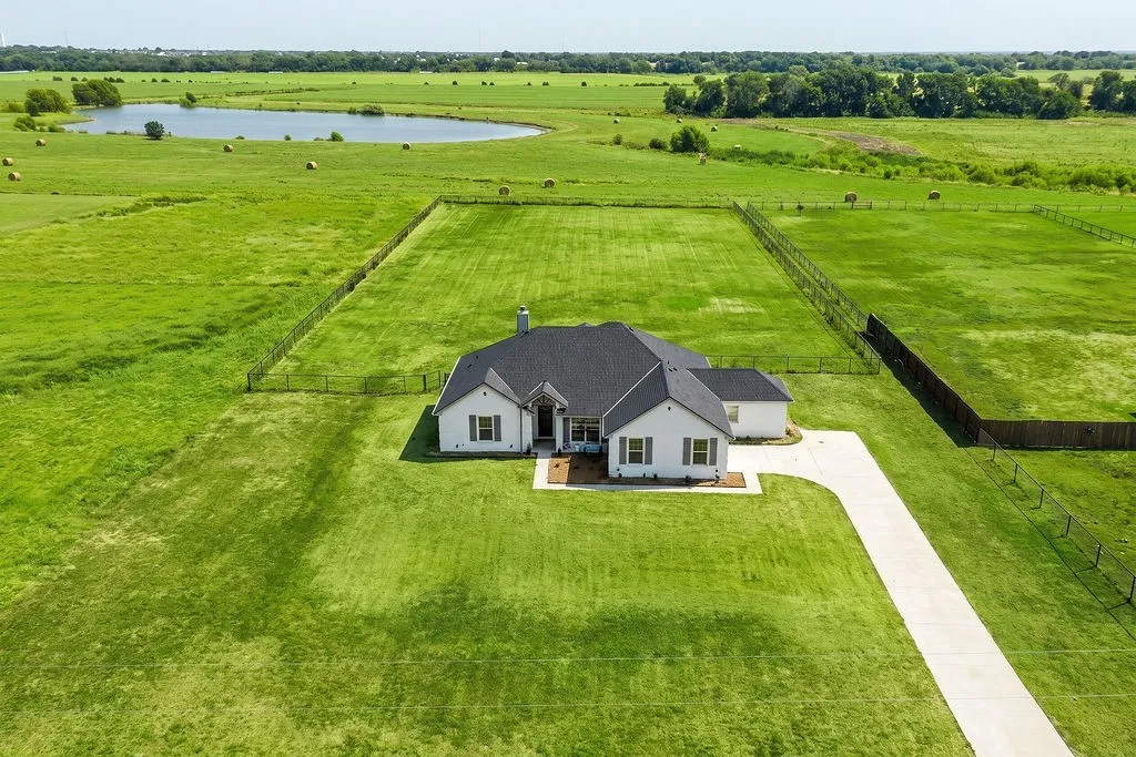 White residence with a dark roof, a long concrete driveway, and a large fenced grassy area