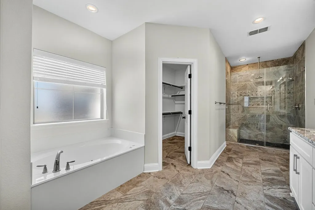 Spacious bathroom featuring a soaking tub, walk-in shower with tile surround, glass enclosure, and a built-in bench