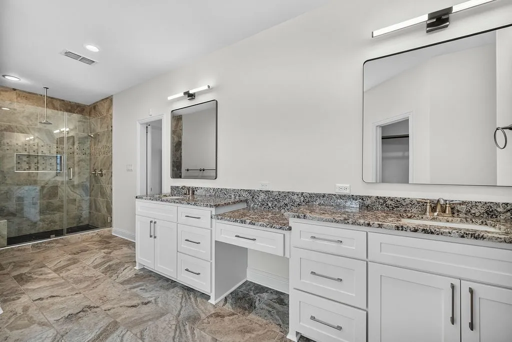 Dual vanity with granite countertops, integrated makeup area, and white shaker-style cabinetry